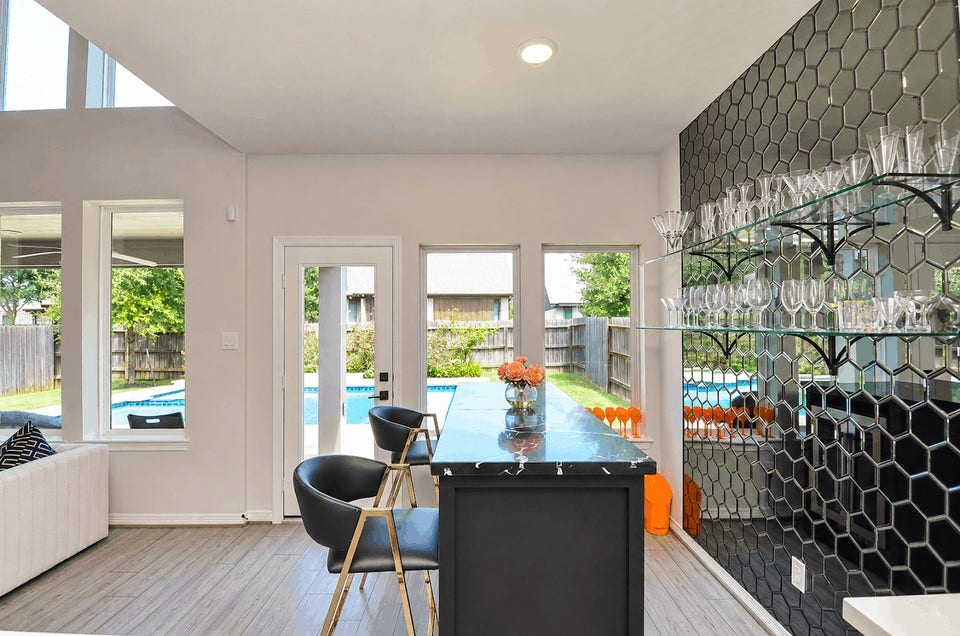 30706 Hawthorn Glen Court, Fulshear, TX 77441 Stylish home bar with sleek black hexagonal backsplash, well-stocked glass shelves, and a chic counter overlooking the backyard pool area. Ideal for entertaining.