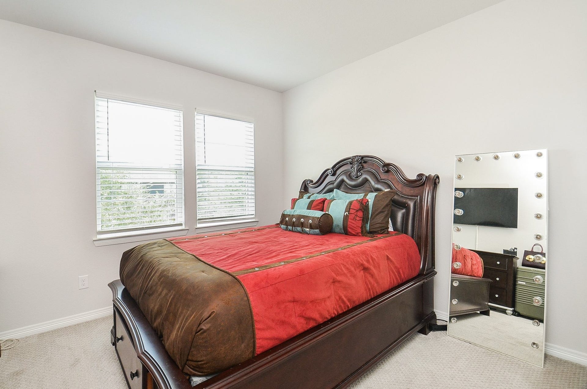 30706 Hawthorn Glen Court, Fulshear, TX 77441 Cozy bedroom featuring a rich, wooden bed frame with elegant detailing, complemented by vibrant bedding and natural light from dual windows, creating a warm and inviting atmosphere.