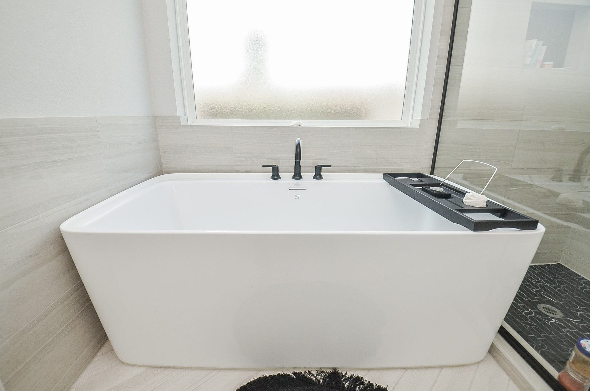 30706 Hawthorn Glen Court, Fulshear, TX 77441 Experience ultimate relaxation in this modern bathroom featuring a sleek, freestanding soaking tub with elegant fixtures, complemented by stylish tile flooring and a frosted window for privacy.
