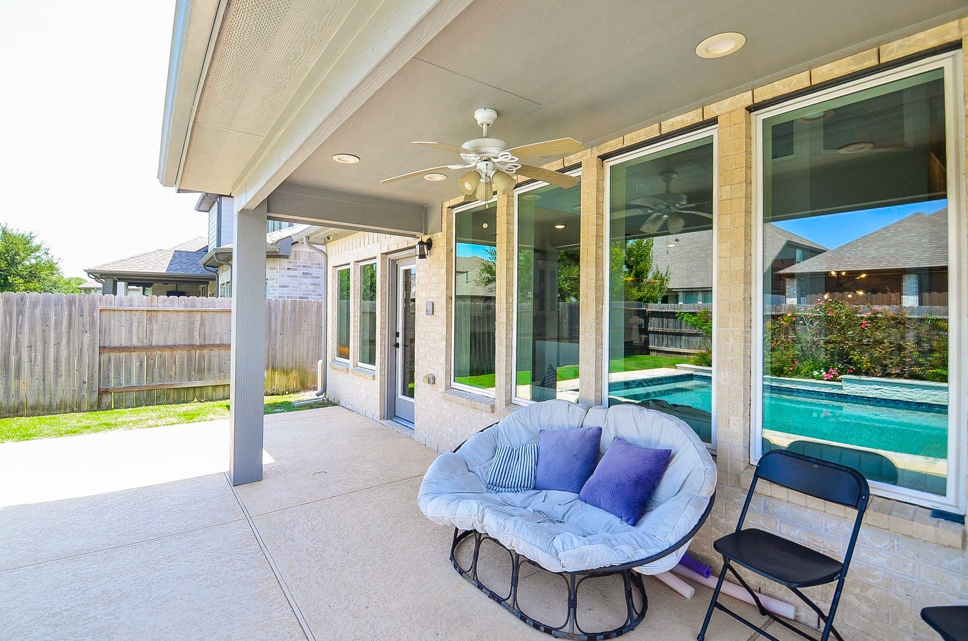 30706 Hawthorn Glen Court, Fulshear, TX 77441 Charming covered patio with a cozy seating area, ceiling fan, and views of the sparkling backyard pool, perfect for relaxation and entertaining.