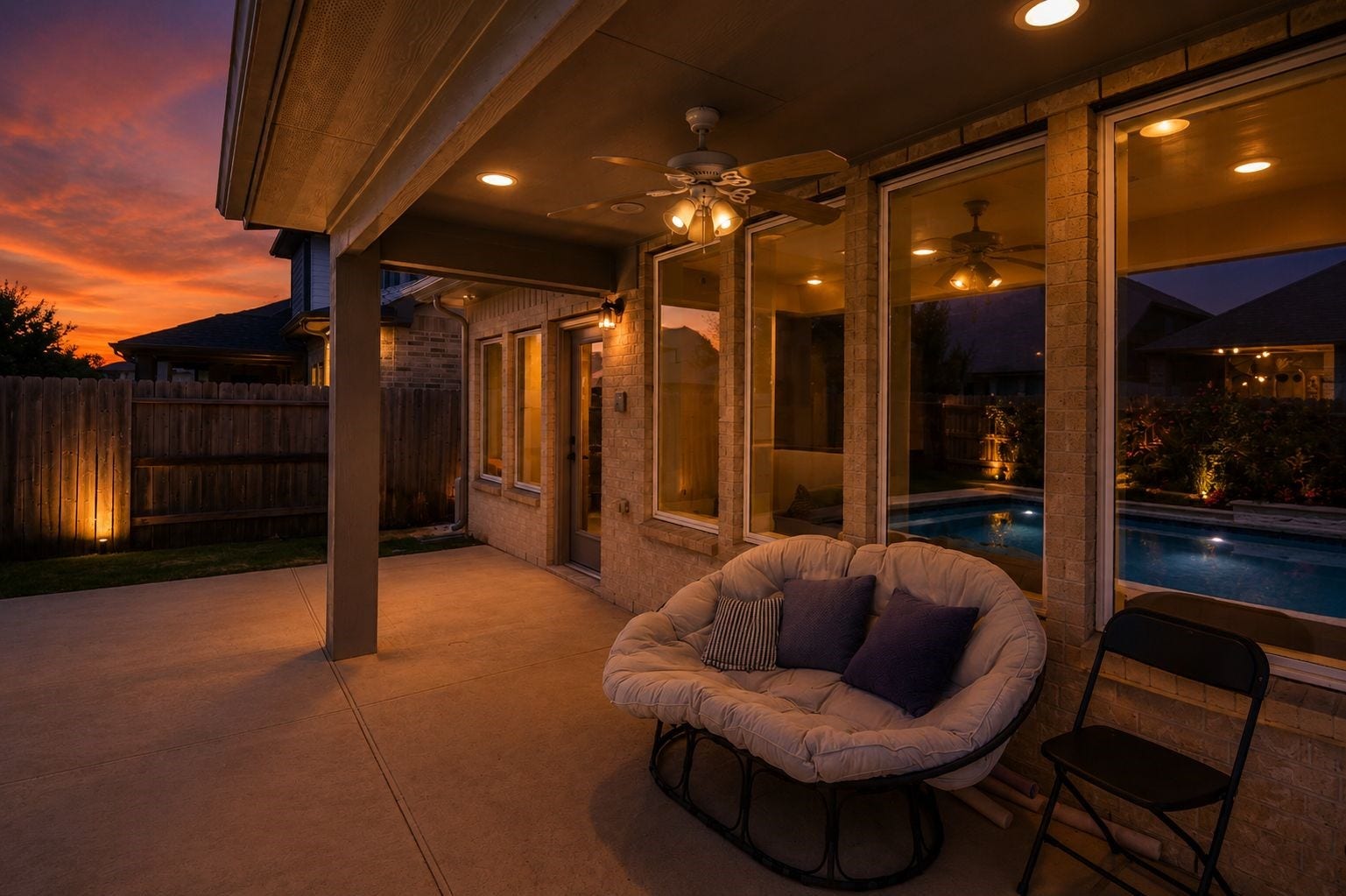 30706 Hawthorn Glen Court, Fulshear, TX 77441 Experience serene evenings on the covered patio, featuring a cozy seating area and ceiling fan, overlooking a beautifully lit pool and sunset views.