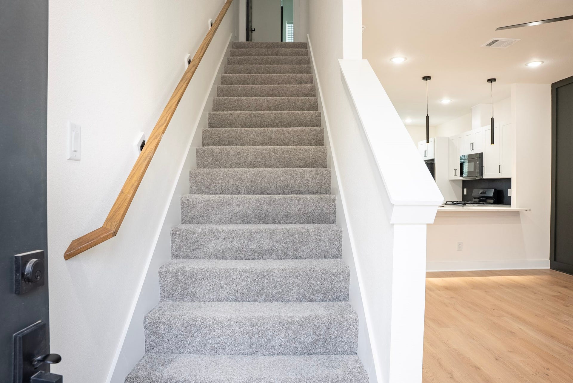 3522 Mansfield Building H Street, #C, Houston, TX 77091 Bright entryway featuring a modern staircase with plush carpeting, leading to an inviting open concept kitchen with sleek white cabinetry and pendant lighting.