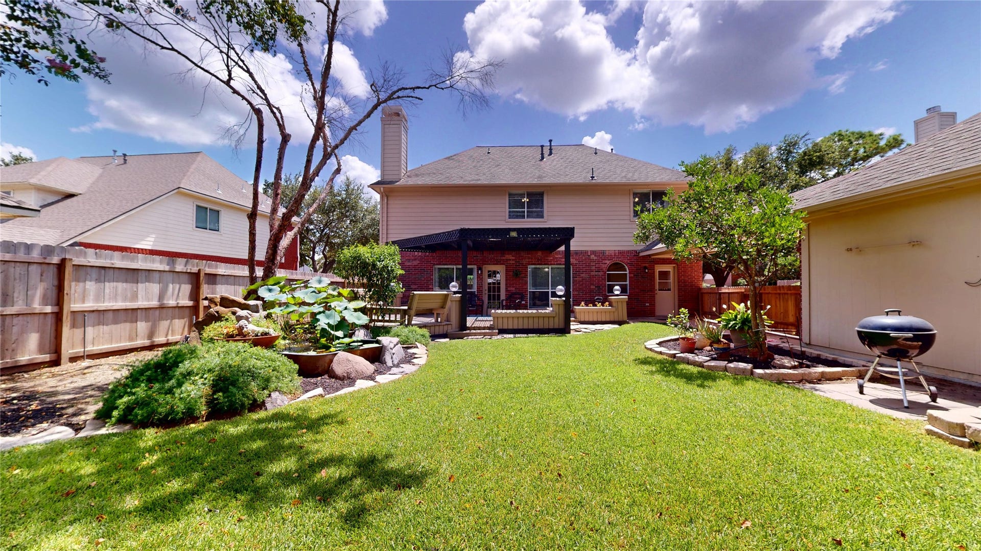 3615 Garrettsville Drive, Pearland, TX 77584 Spacious backyard oasis featuring a stylish pergola-covered deck with built-in benches, koi fish pond, lush green lawn, and charming garden beds, perfect for outdoor relaxation and entertaining.