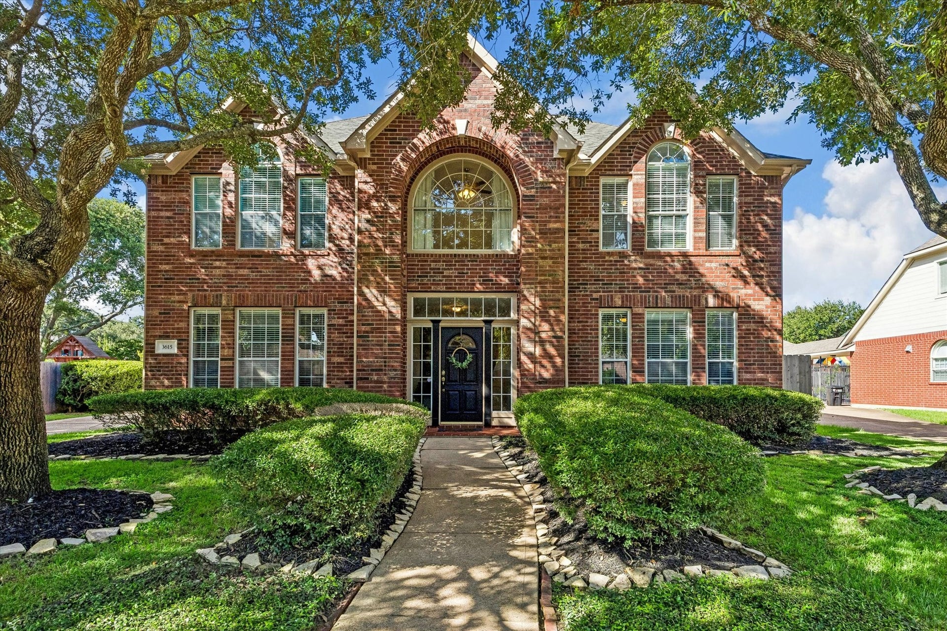 3615 Garrettsville Drive, Pearland, TX 77584 Stately brick home with charming arched windows, surrounded by lush landscaping and mature trees, offering inviting curb appeal.