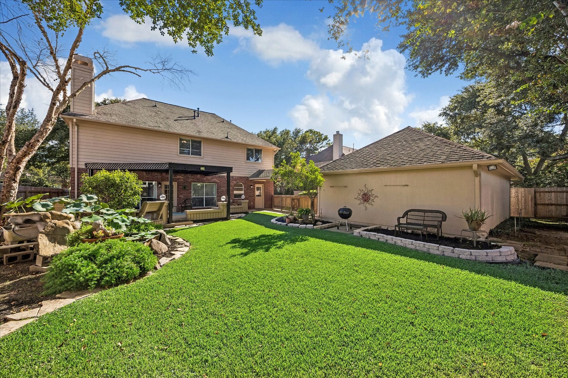 3615 Garrettsville Drive, Pearland, TX 77584 Spacious backyard oasis featuring a stylish pergola-covered deck with built-in benches, koi fish pond, lush green lawn, and charming garden beds, perfect for outdoor relaxation and entertaining.