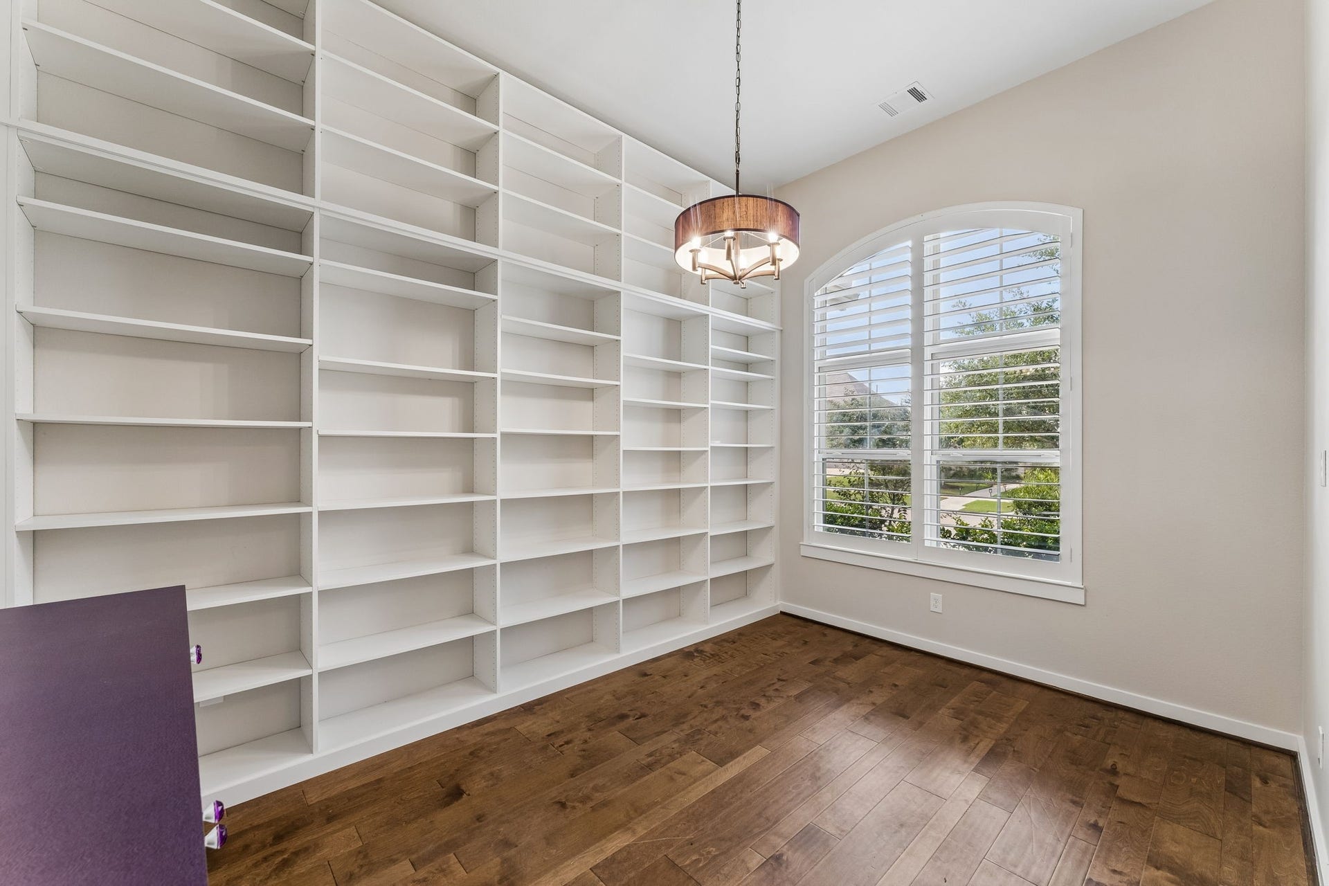 30410 Myrtle Oak Drive, Fulshear, TX 77423 Elevated private home office featuring extensive custom built-ins, elegant plantation shutters, and a modern chandelier, creating the perfect productive and sophisticated workspace.