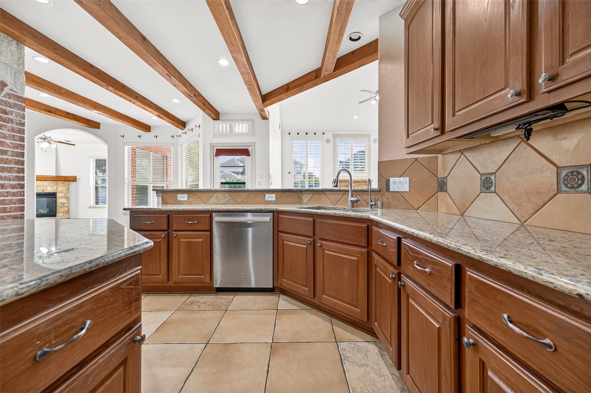 11803 Silverwood Bend Lane, Cypress, TX 77433 Spacious kitchen with elegant wooden cabinets, granite countertops, and stainless steel appliances, accented by exposed beams and natural light from large windows.
