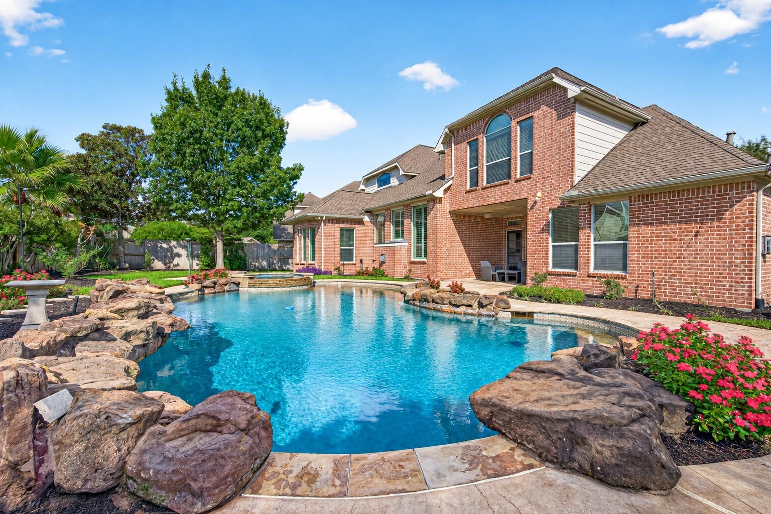 11803 Silverwood Bend Lane, Cypress, TX 77433 Stunning backyard oasis featuring a sparkling pool with natural stone accents, surrounded by lush landscaping and a beautiful brick home as the backdrop.