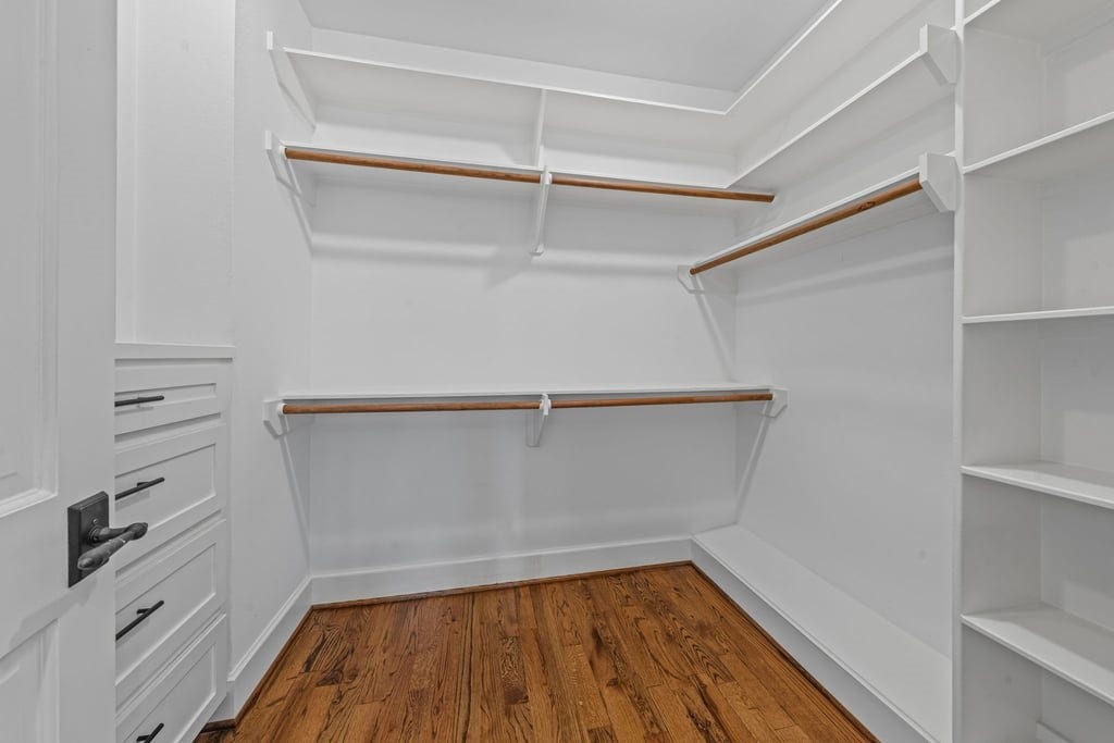 Spacious primary walk-in closet with built-in shelving and multiple hanging areas.