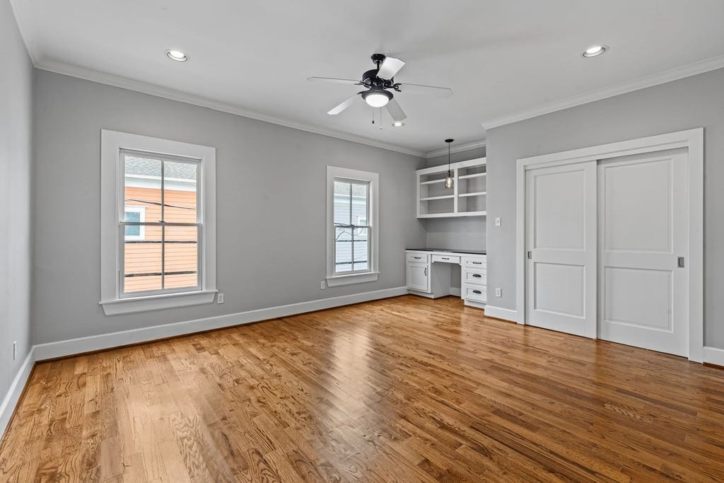 Generously proportioned primary bedroom with hardwood flooring and custom built-in shelving.