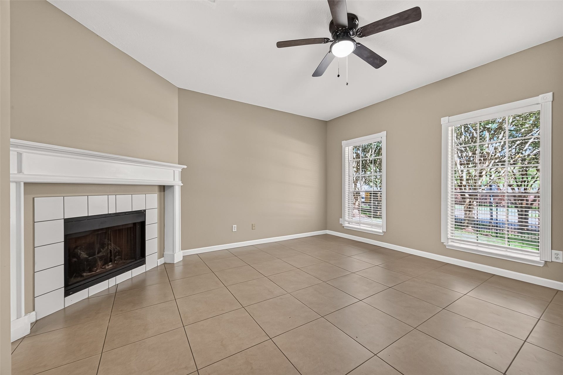 2930 Grants Lake Boulevard, #2202, Sugar Land, TX 77479 Inviting living room featuring a fireplace with decorative mantel, tile flooring, ceiling fan, and large windows overlooking the landscaped surroundings.