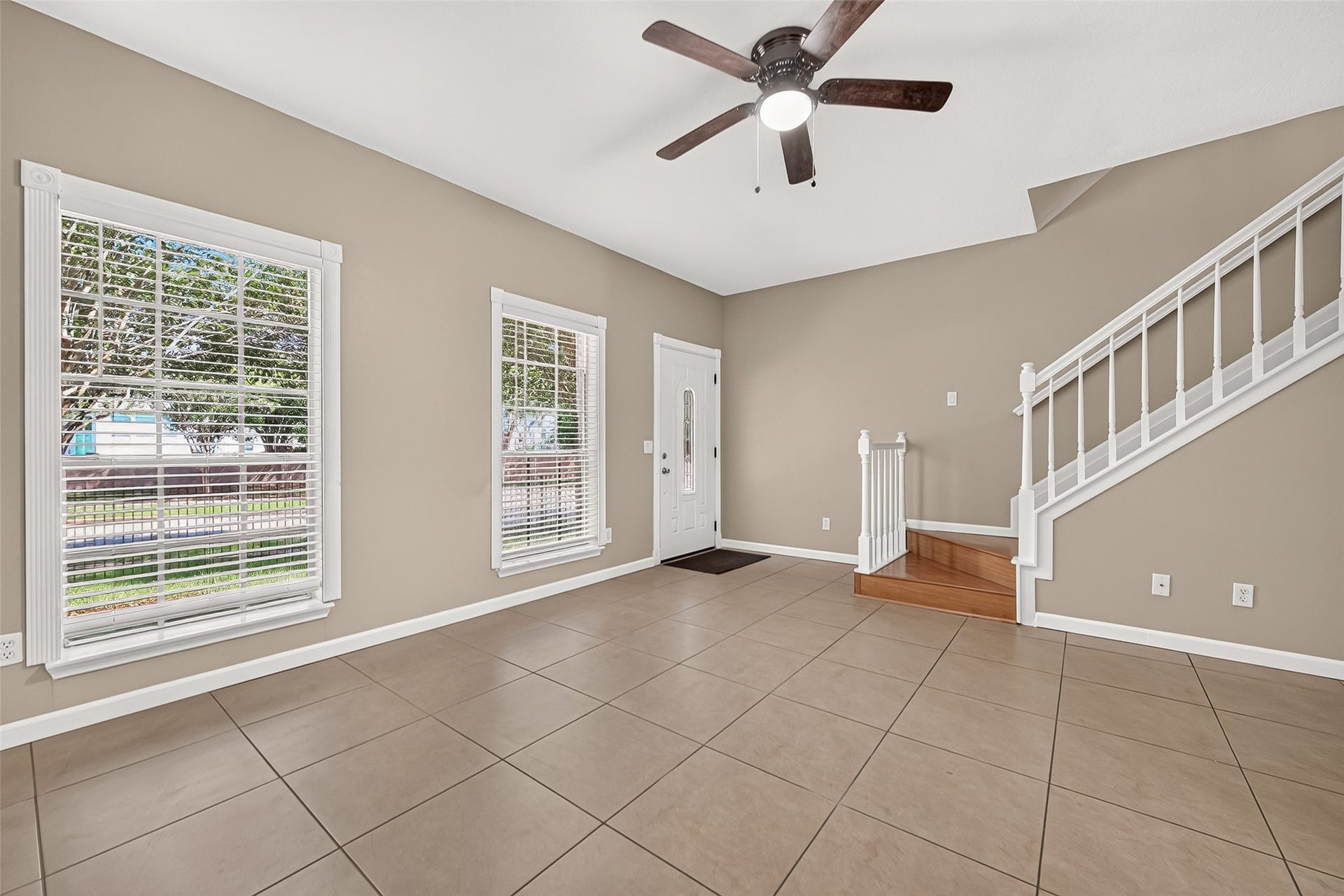 2930 Grants Lake Boulevard, #2202, Sugar Land, TX 77479 Spacious living area with tile flooring, ceiling fan, abundant natural light, and an attractive wood staircase with white railing.