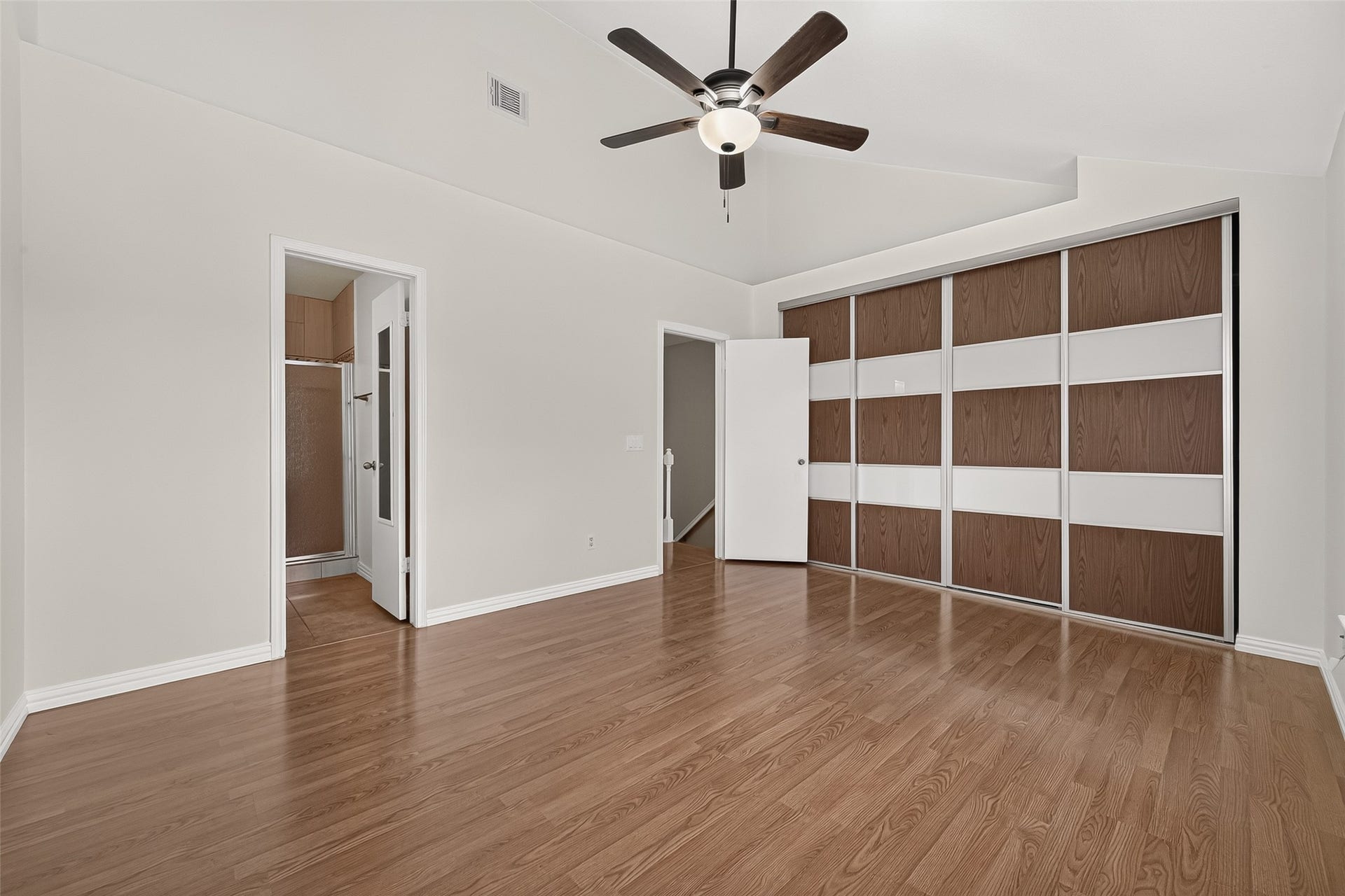 2930 Grants Lake Boulevard, #2202, Sugar Land, TX 77479 Spacious primary bedroom featuring wood-look flooring, vaulted ceiling, ceiling fan, en-suite bath access, and newly installed premium sliding closet doorsa significant recent upgrade.