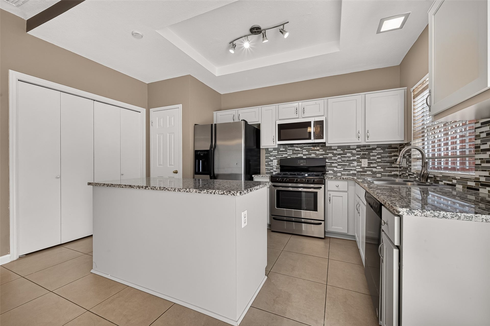 2930 Grants Lake Boulevard, #2202, Sugar Land, TX 77479 Bright kitchen with granite-topped island, stainless-steel appliances, white cabinetry, tile flooring, and contemporary lighting.