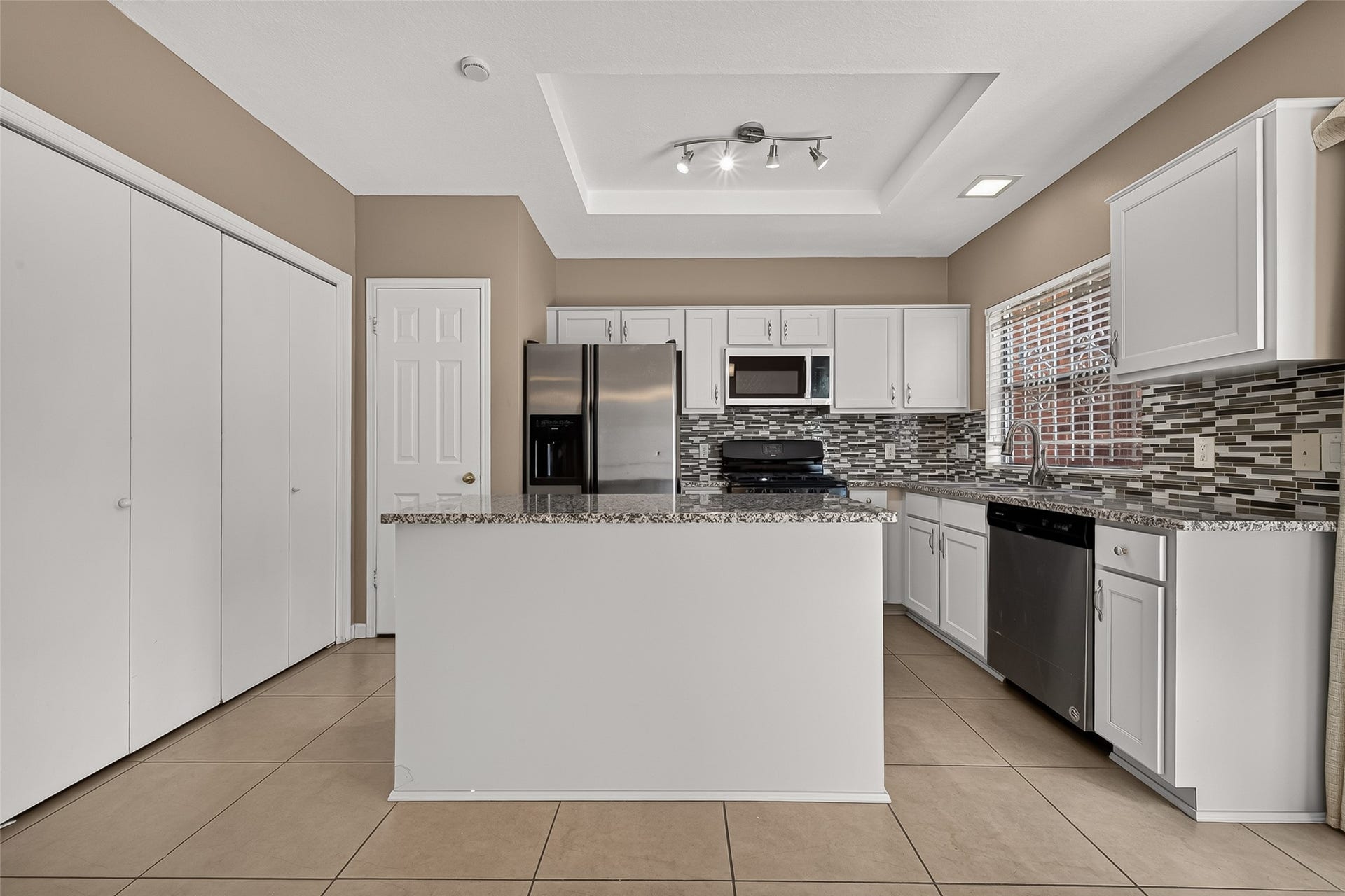 2930 Grants Lake Boulevard, #2202, Sugar Land, TX 77479 Spacious kitchen featuring granite countertops, center island, white cabinetry, tile backsplash, stainless-steel refrigerator and microwave, and ample cabinet and counter space.