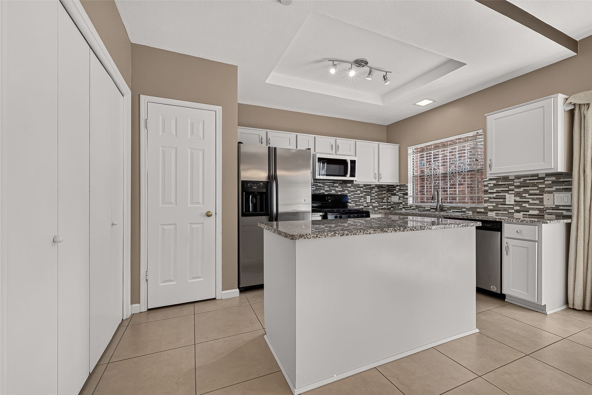 2930 Grants Lake Boulevard, #2202, Sugar Land, TX 77479 Another view highlighting the generous granite-topped center island, abundant cabinetry, stainless-steel appliances, decorative backsplash, and tray ceiling with contemporary lighting.