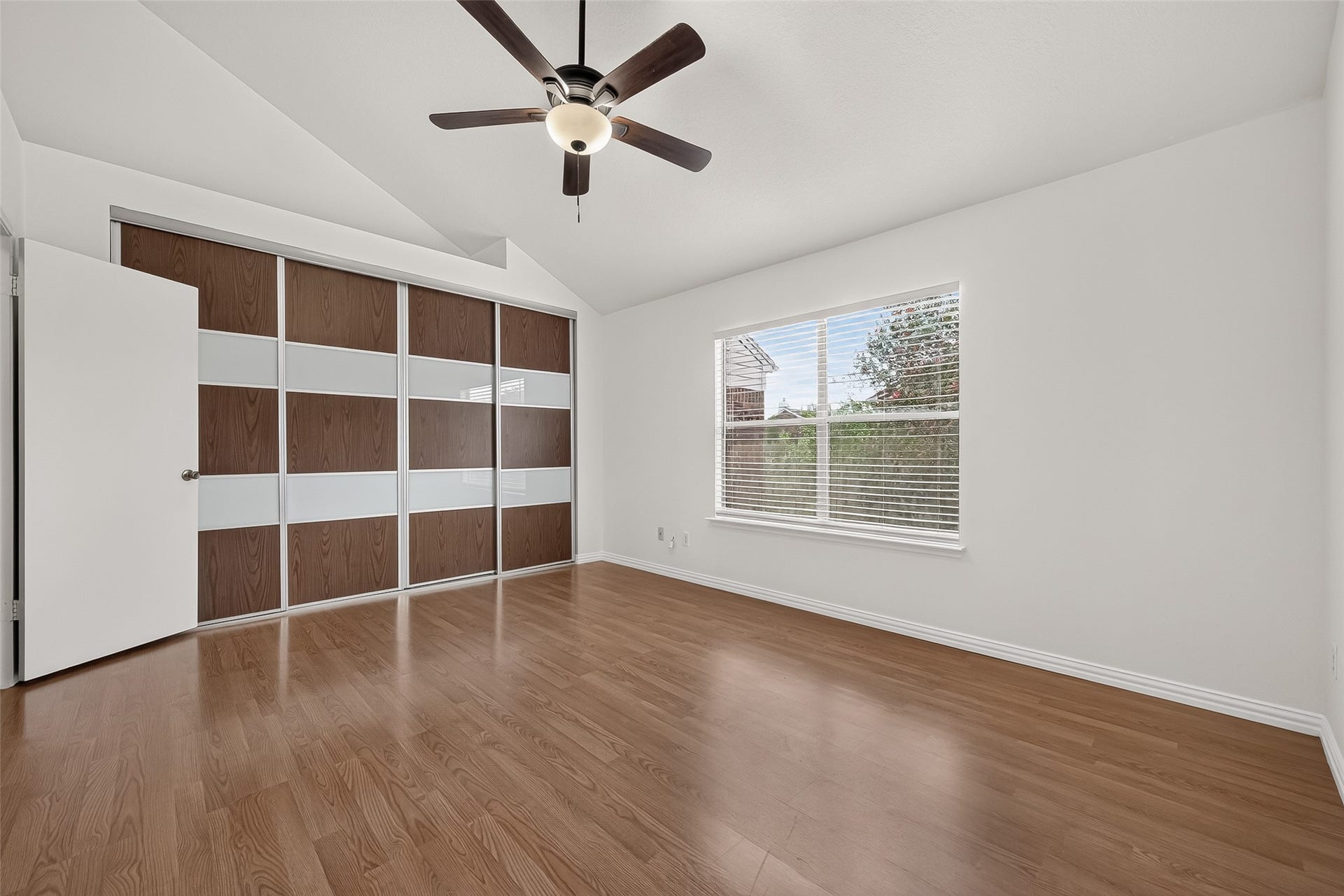 2930 Grants Lake Boulevard, #2202, Sugar Land, TX 77479 Bright primary bedroom with vaulted ceiling, large window, wood-look flooring, and impressive newly installed sliding closet doors providing a clean, contemporary look.