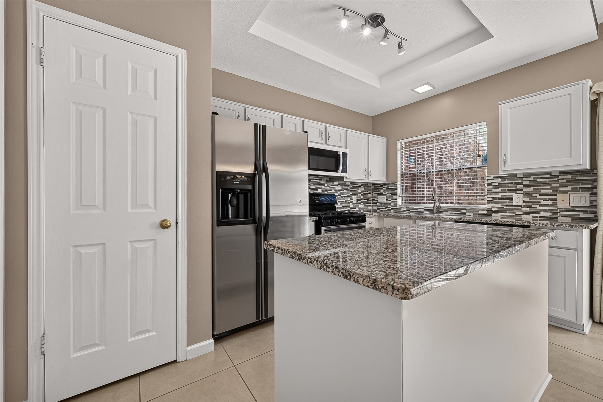2930 Grants Lake Boulevard, #2202, Sugar Land, TX 77479 Open kitchen and dining area featuring a large granite island, white cabinetry, tile flooring, modern lighting, and convenient access to the private patio.