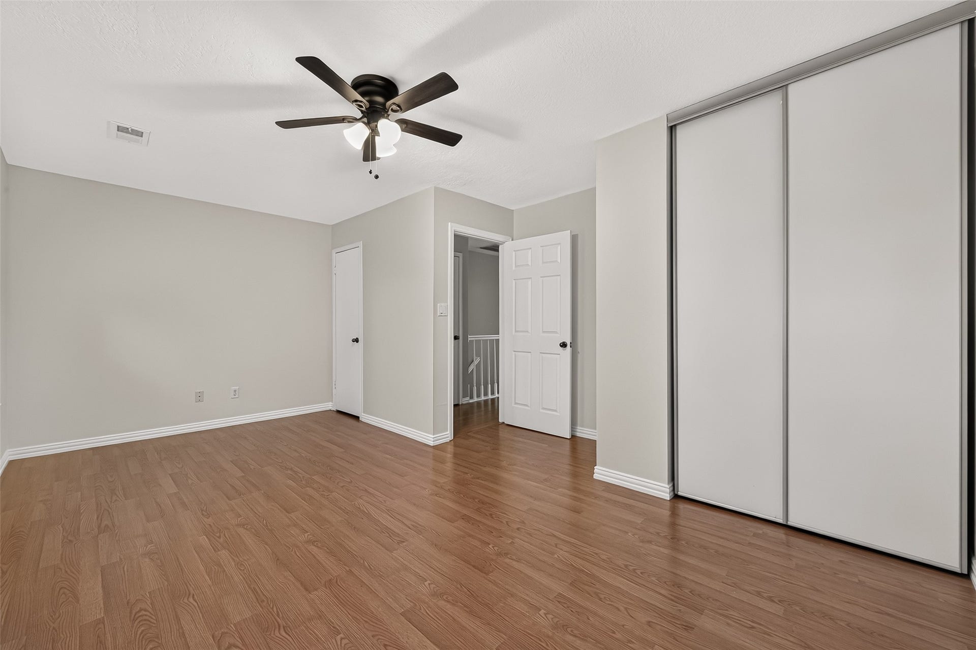 2930 Grants Lake Boulevard, #2202, Sugar Land, TX 77479 Spacious secondary bedroom featuring wood-look flooring, ceiling fan, and newly installed contemporary sliding closet doors providing a clean, updated appearance.