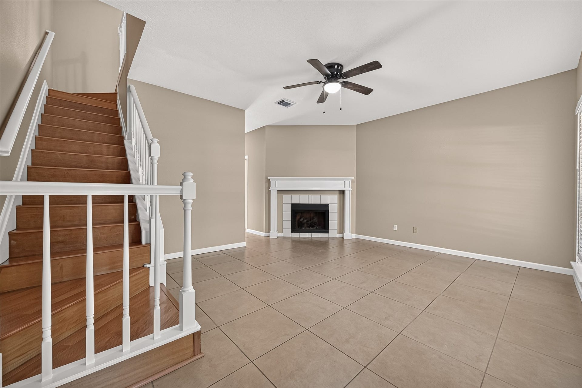 2930 Grants Lake Boulevard, #2202, Sugar Land, TX 77479 Open living area featuring tile flooring, fireplace, ceiling fan, neutral finishes, and attractive wood staircase with white railing leading to the second floor.