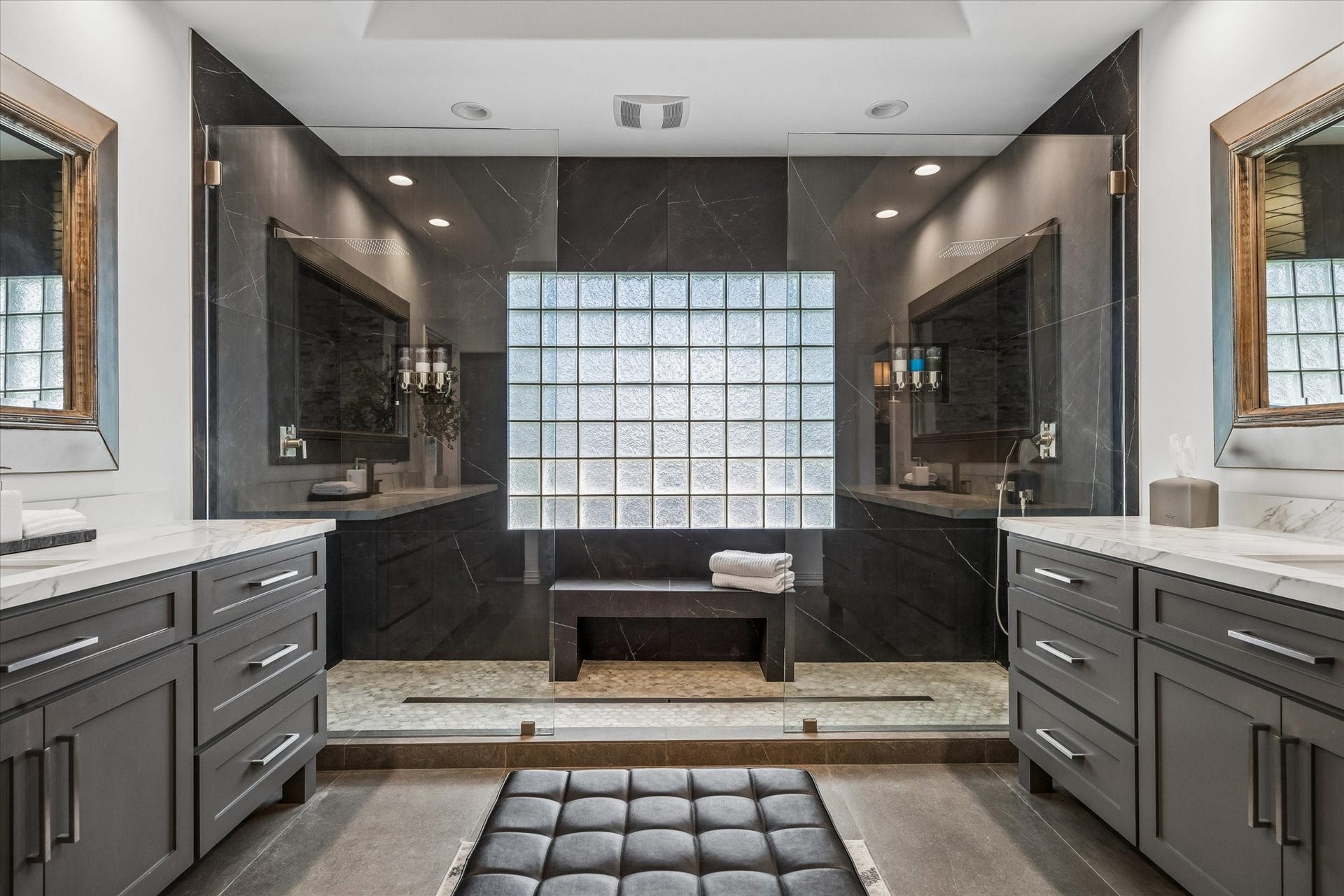 Oversized doorless walk-in shower with Carrera tile flooring, dual rain showerheads, full-height shower porcelain tile, and a glass-block window that provides natural light and privacy.