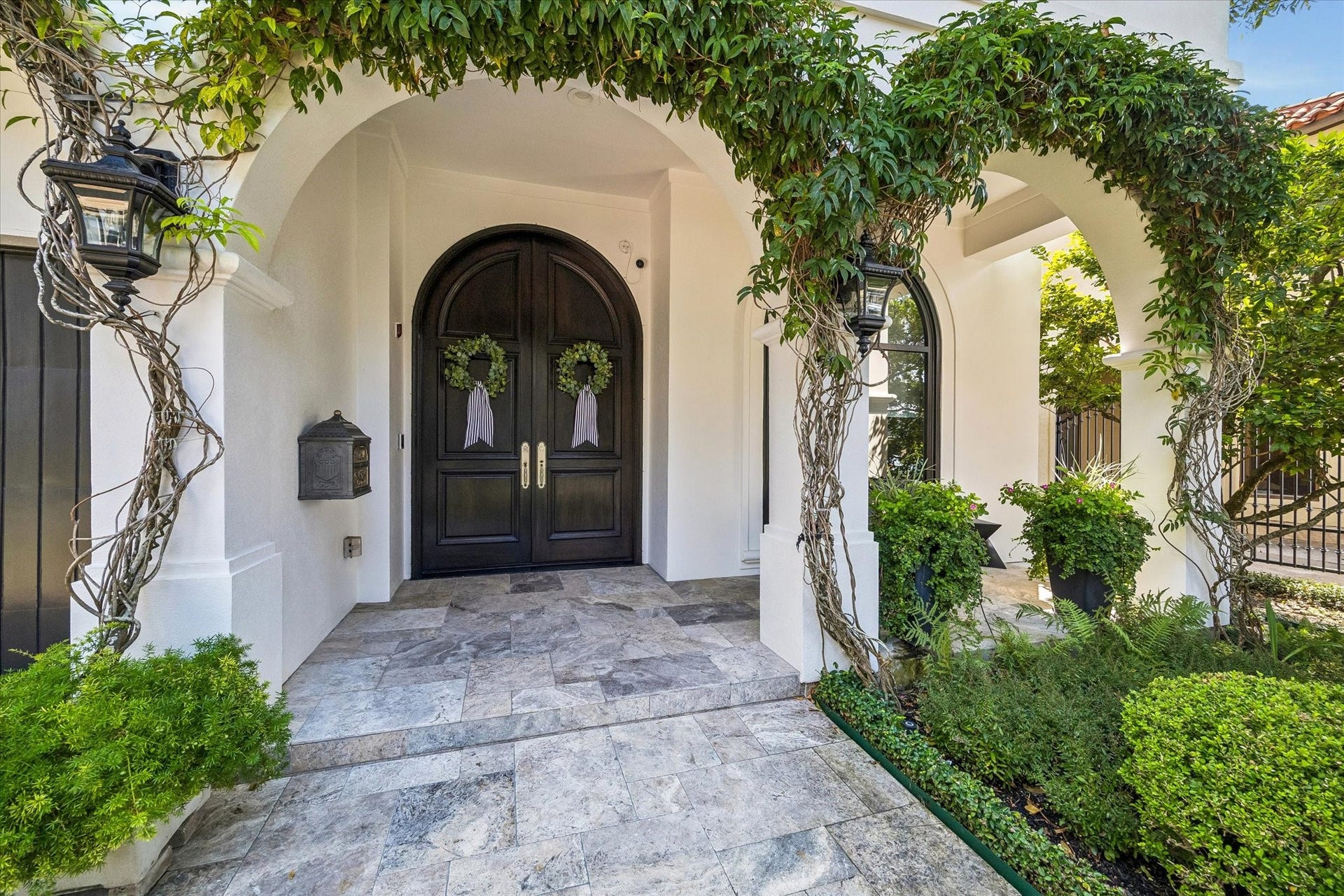 Inviting front porch featuring arched entryways, climbing vines, and a double front door.