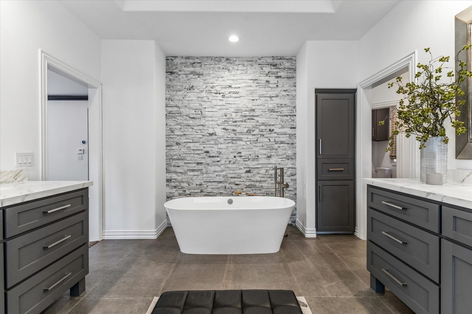 Beautiful freestanding soaker tub afront floor-to-ceiling laddered marble accent wall.
