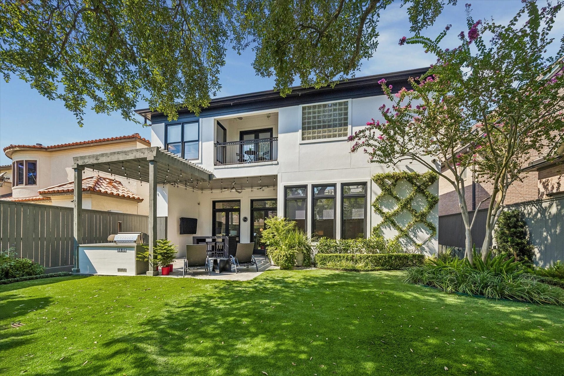 Beautifully landscaped backyard with low-maintenance turf, mature trees, and plenty of room to play. An outdoor kitchen and pergola-covered patio offer a welcoming setting for dining and relaxing outdoors.