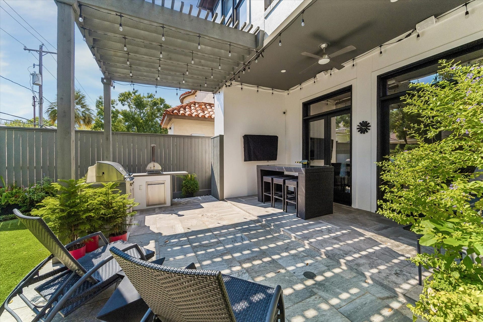 The redwood pergola with bistro lights add shade and charm to the patio, creating an inviting spot to relax and watch TV outdoors.