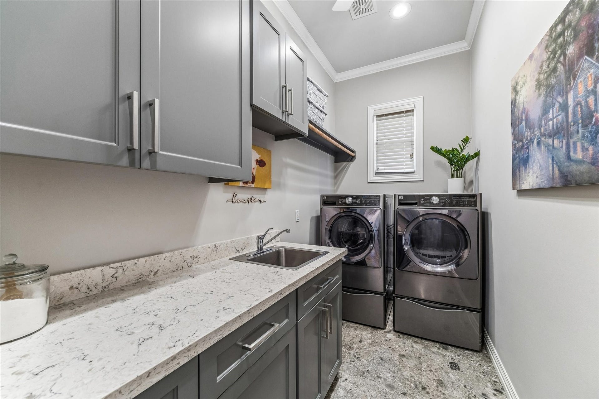 Well-equipped laundry room with space for a full-sized washer and dryer, ample storage, hanging rod, and a sink.