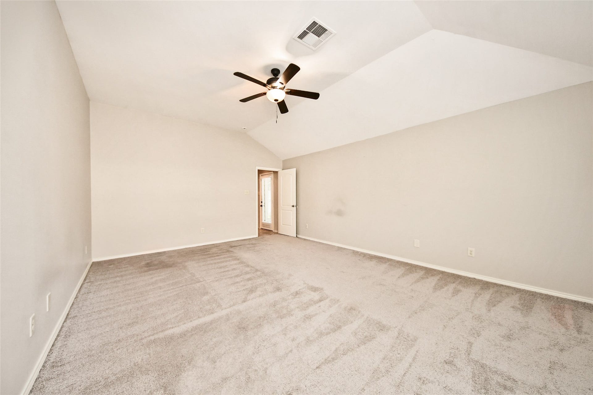 Spacious bedroom with vaulted ceiling, neutral tones, plush carpeting, and a modern ceiling fan.