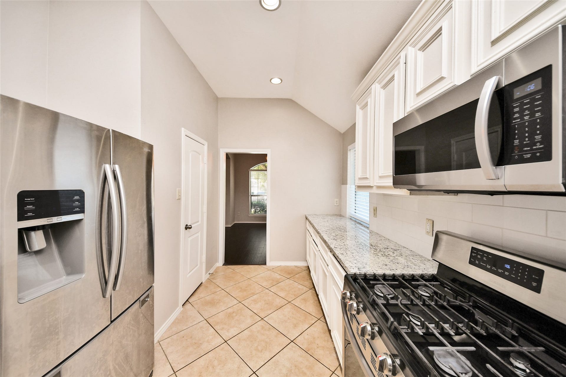 Modern kitchen featuring stainless steel appliances, granite countertops, and elegant white cabinetry, complemented by a sleek tile floor.