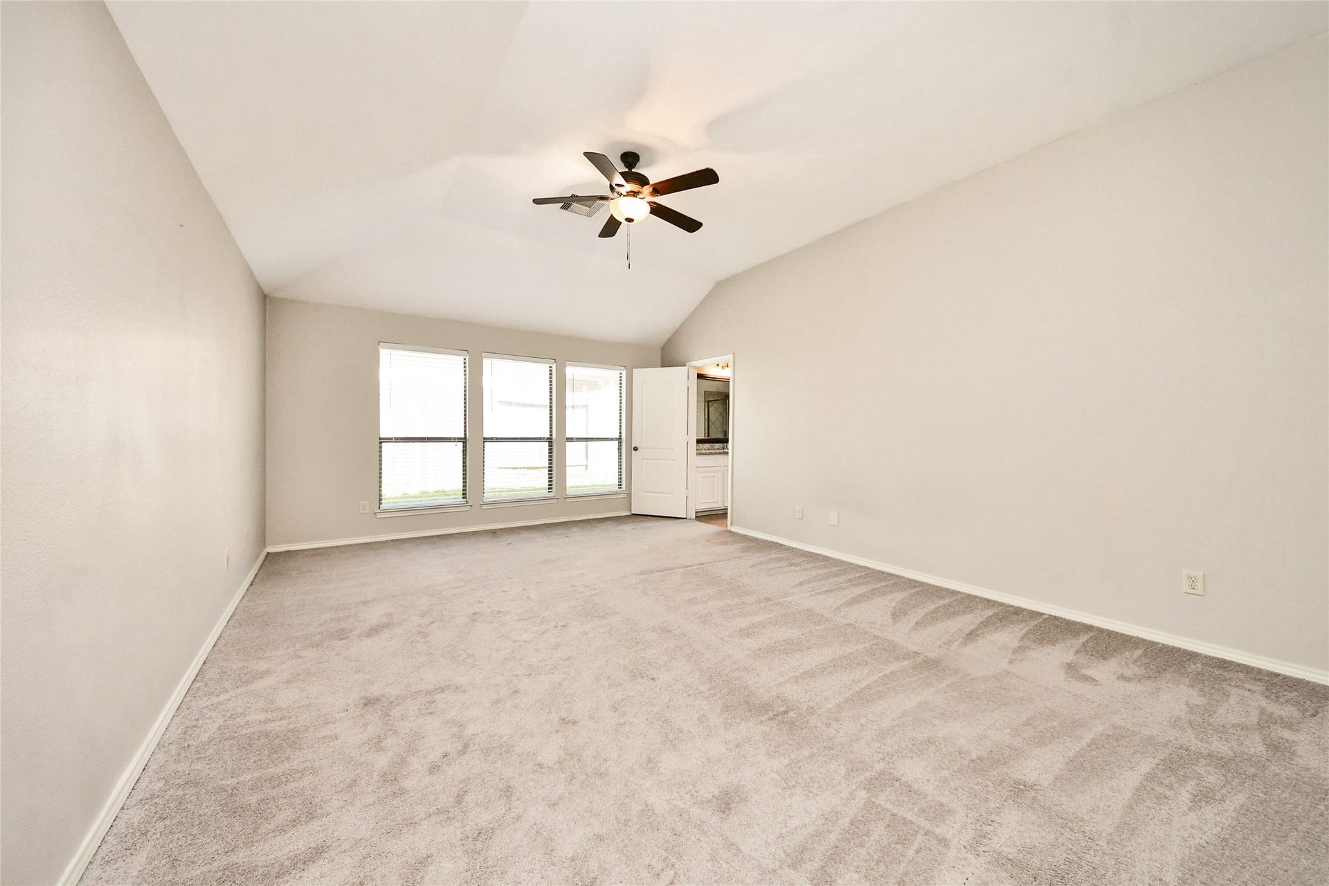 Spacious living area with vaulted ceilings, a modern ceiling fan, and large windows offering abundant natural light.