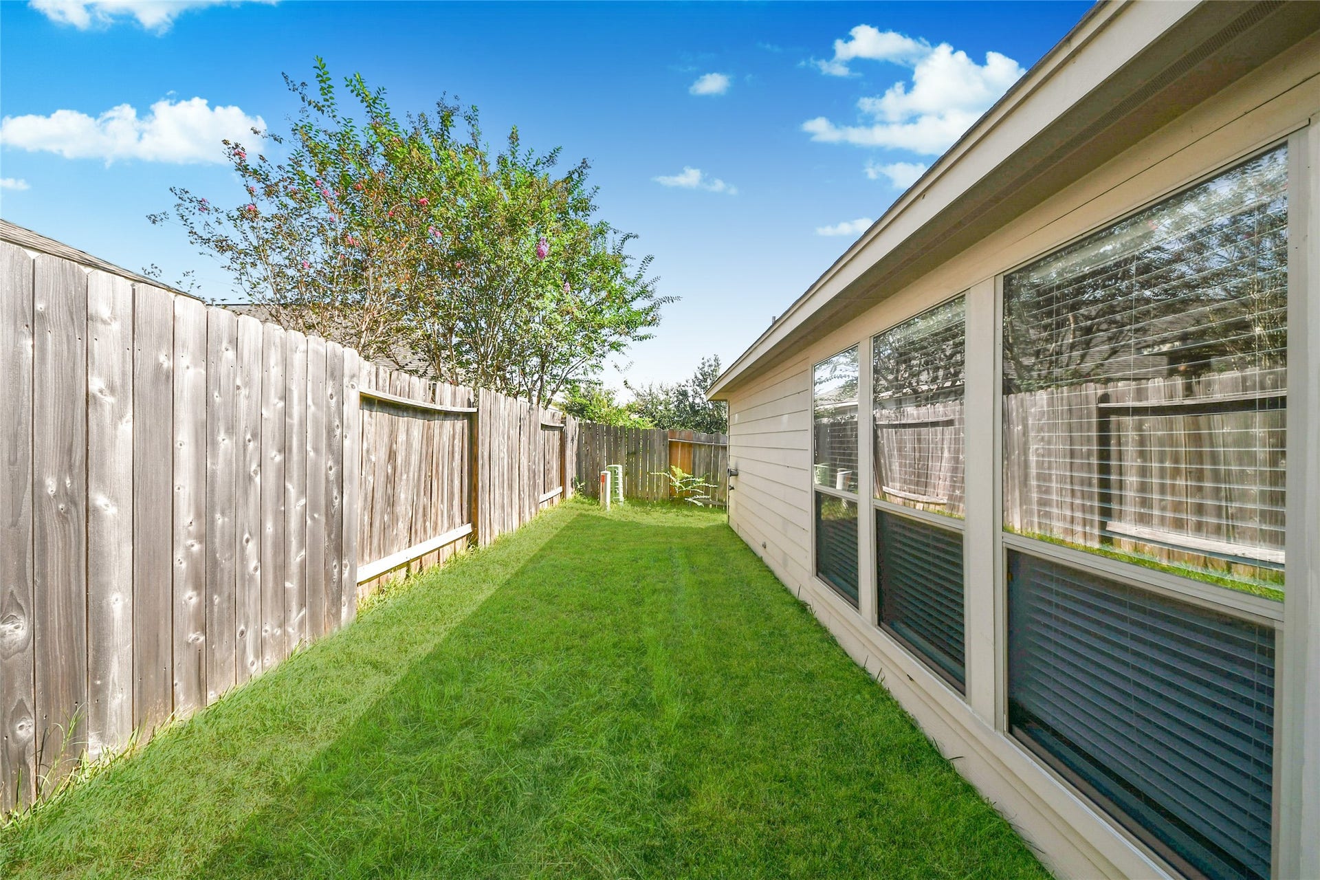 Charming side yard with lush grass, bordered by a wooden fence, perfect for a private outdoor retreat.