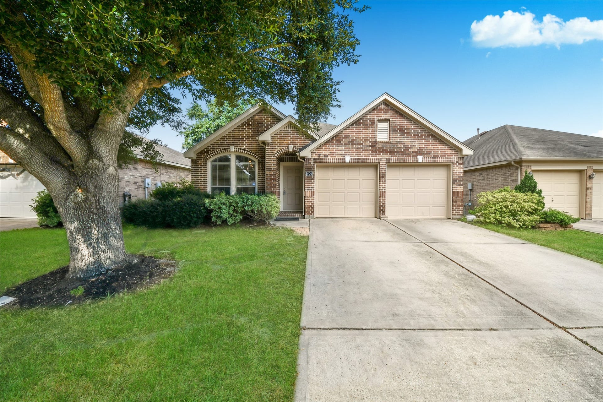 Charming brick home with a two-car garage and a well-maintained front lawn, accented by mature trees and lush landscaping for excellent curb appeal.