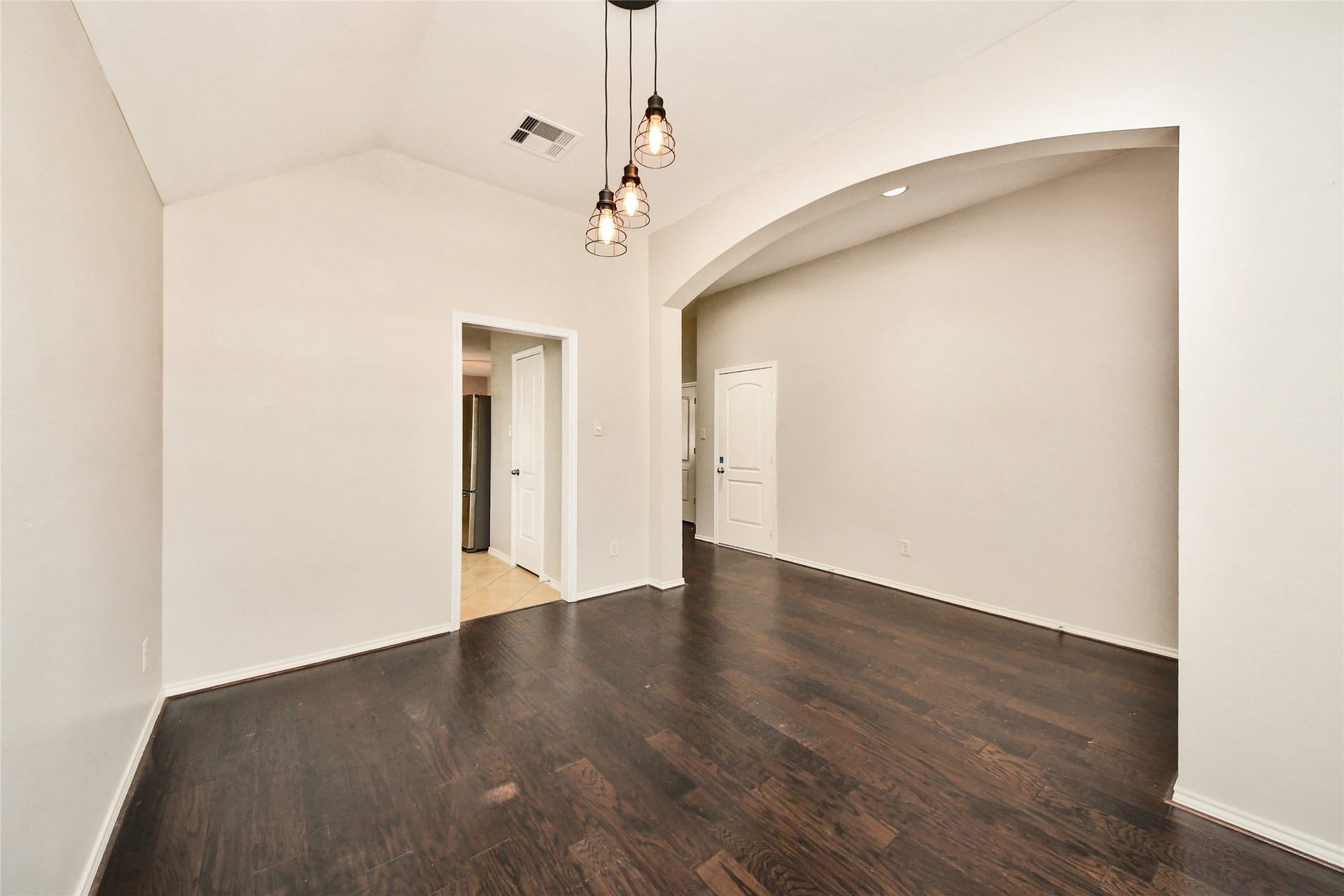 Spacious room with vaulted ceilings, elegant dark hardwood floors, and chic pendant lighting, leading to adjacent areas through stylish archways.