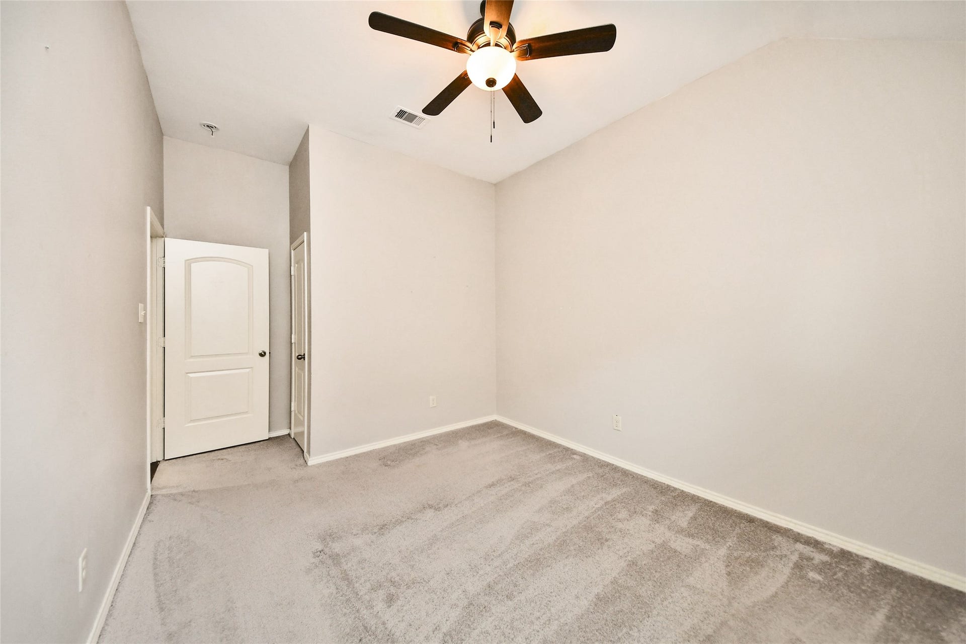 Cozy bedroom with soft carpeting and neutral walls, featuring a ceiling fan for comfort and a classic white door entry.