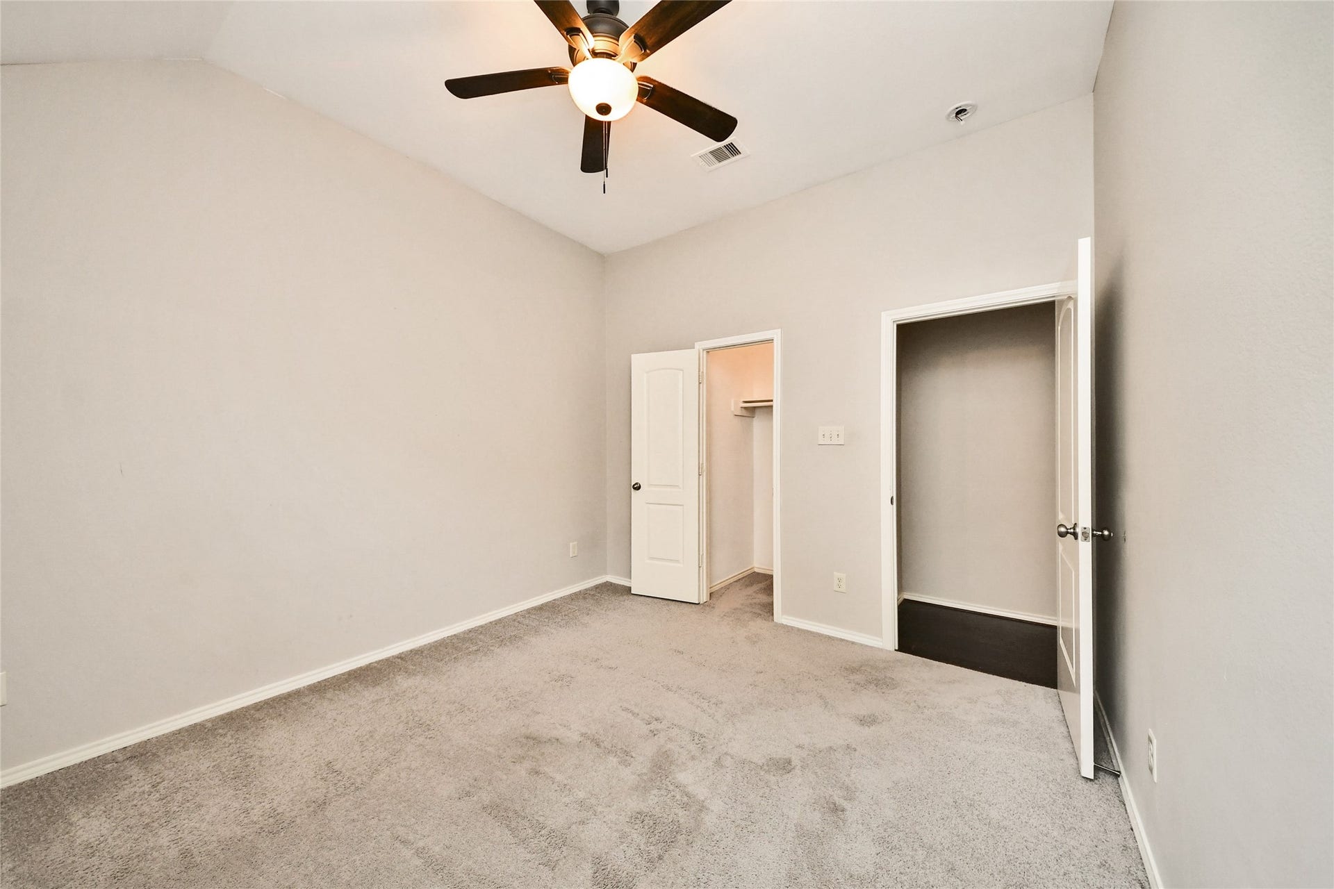 Spacious bedroom featuring plush carpeting, neutral walls, a ceiling fan, and an adjoining walk-in closet for ample storage.