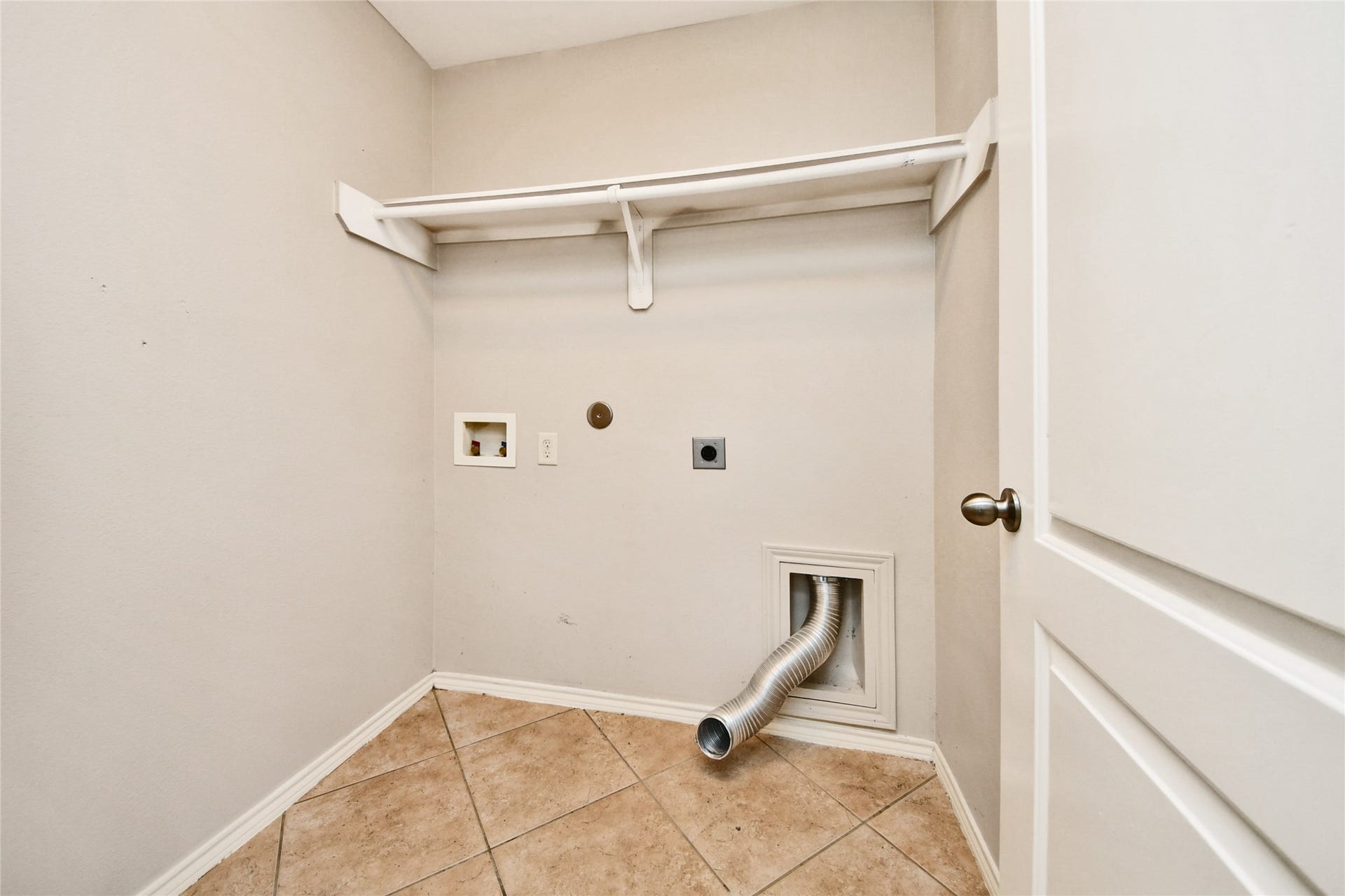 Spacious laundry room with tile flooring, ample storage shelf, and hookups for washer and dryer.