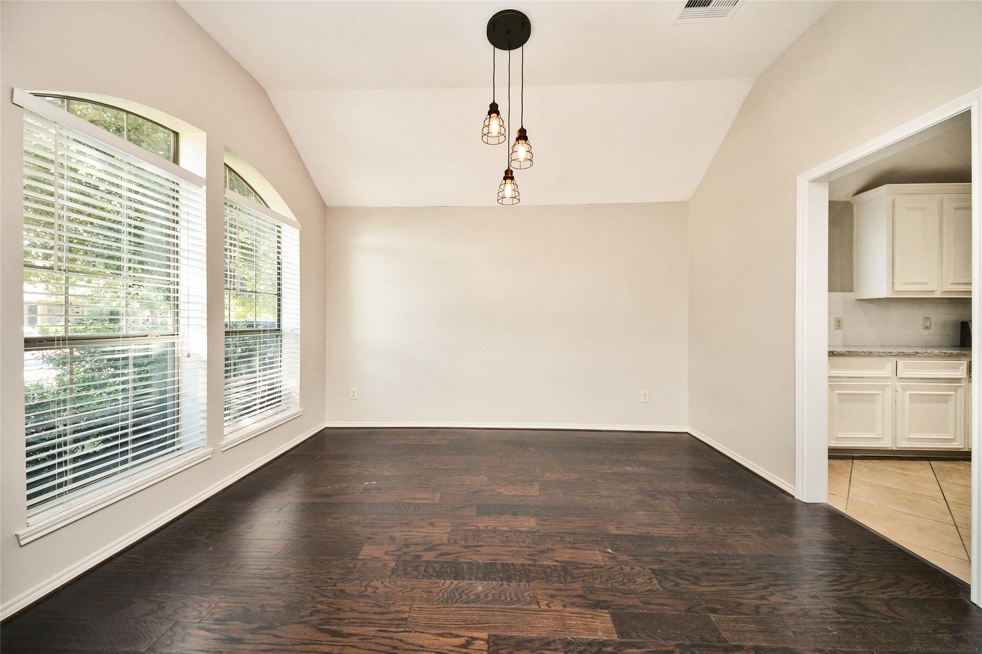 Bright dining area with rich hardwood floors, large arched windows for natural light, and elegant pendant lighting, seamlessly connected to the kitchen.
