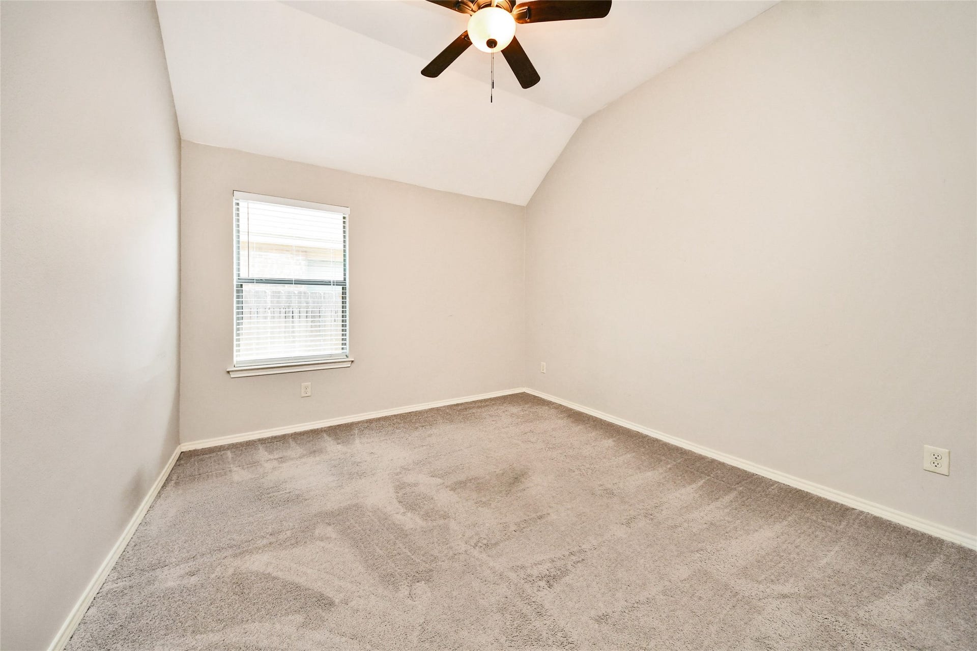 Spacious bedroom with plush carpeting, vaulted ceiling, and natural light from a single window, enhanced by a modern ceiling fan.
