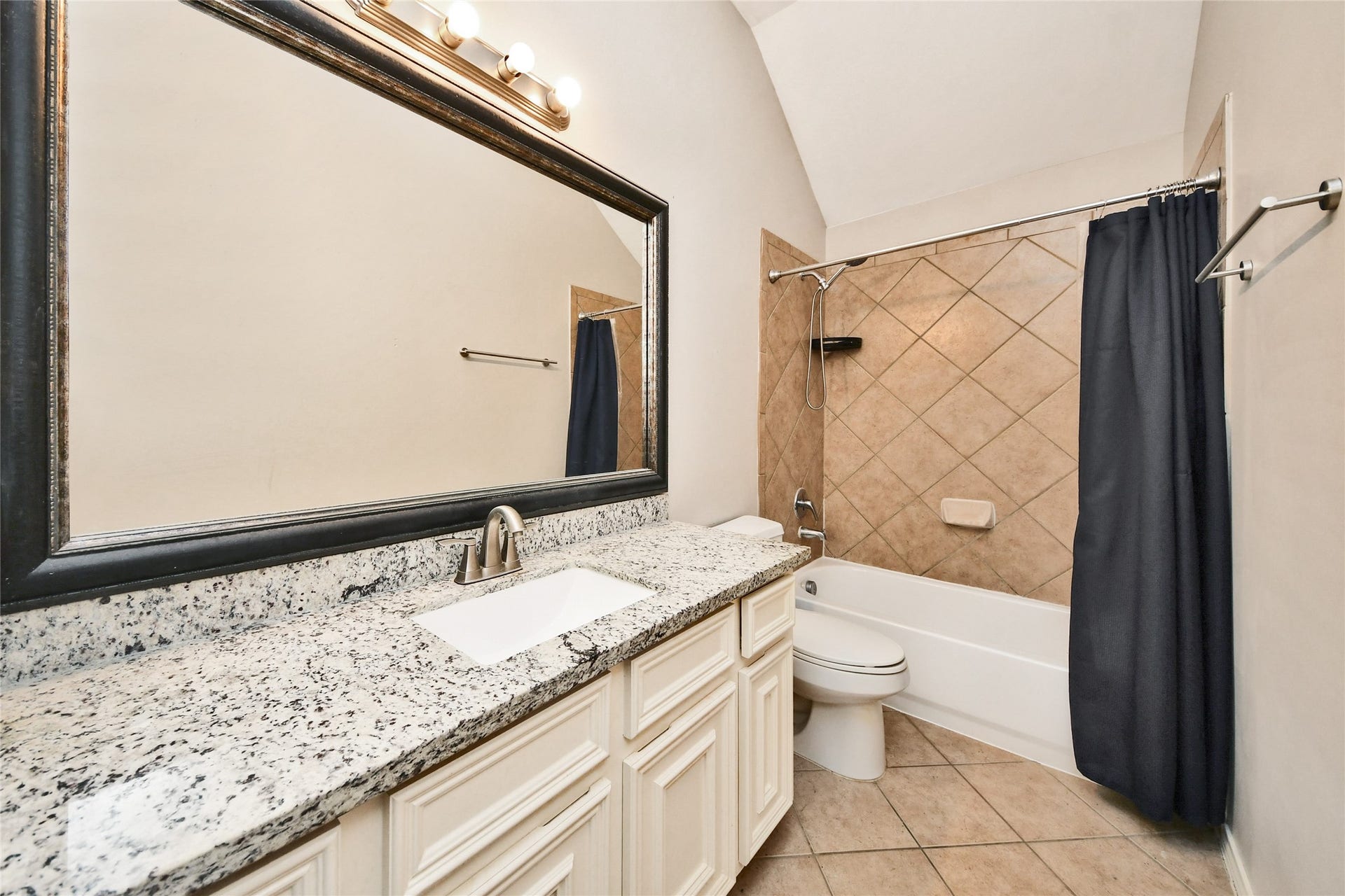 Elegant bathroom featuring a granite countertop, large framed mirror, and a tiled shower with a sleek curtain.