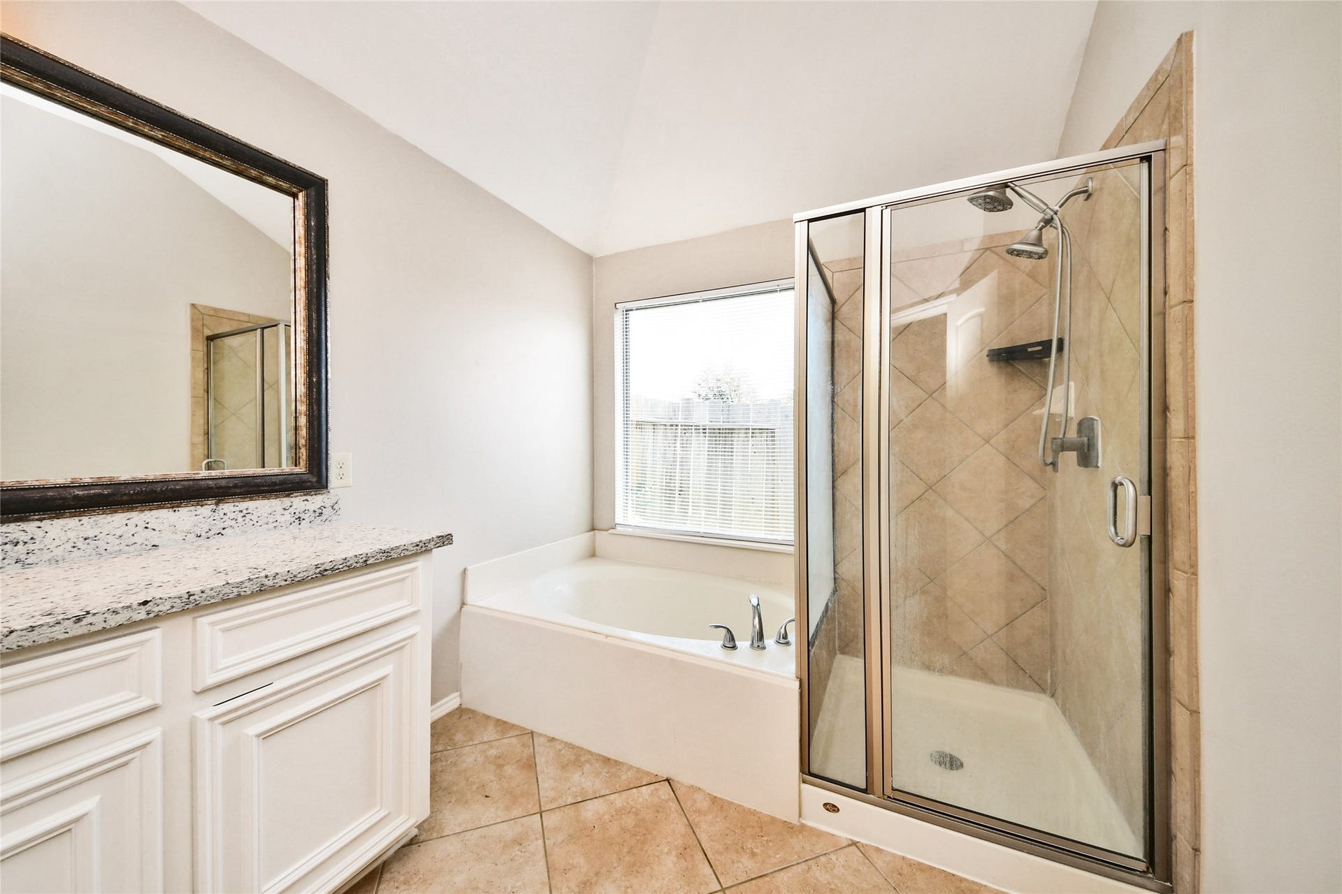 Elegant bathroom featuring a spacious glass-enclosed shower, luxurious soaking tub, and a granite-topped vanity, all bathed in natural light.