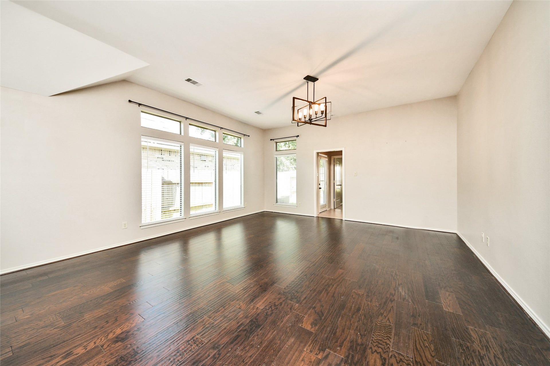 Spacious living area with rich hardwood floors, abundant natural light from large windows, and a modern light fixture, perfect for comfortable gatherings.
