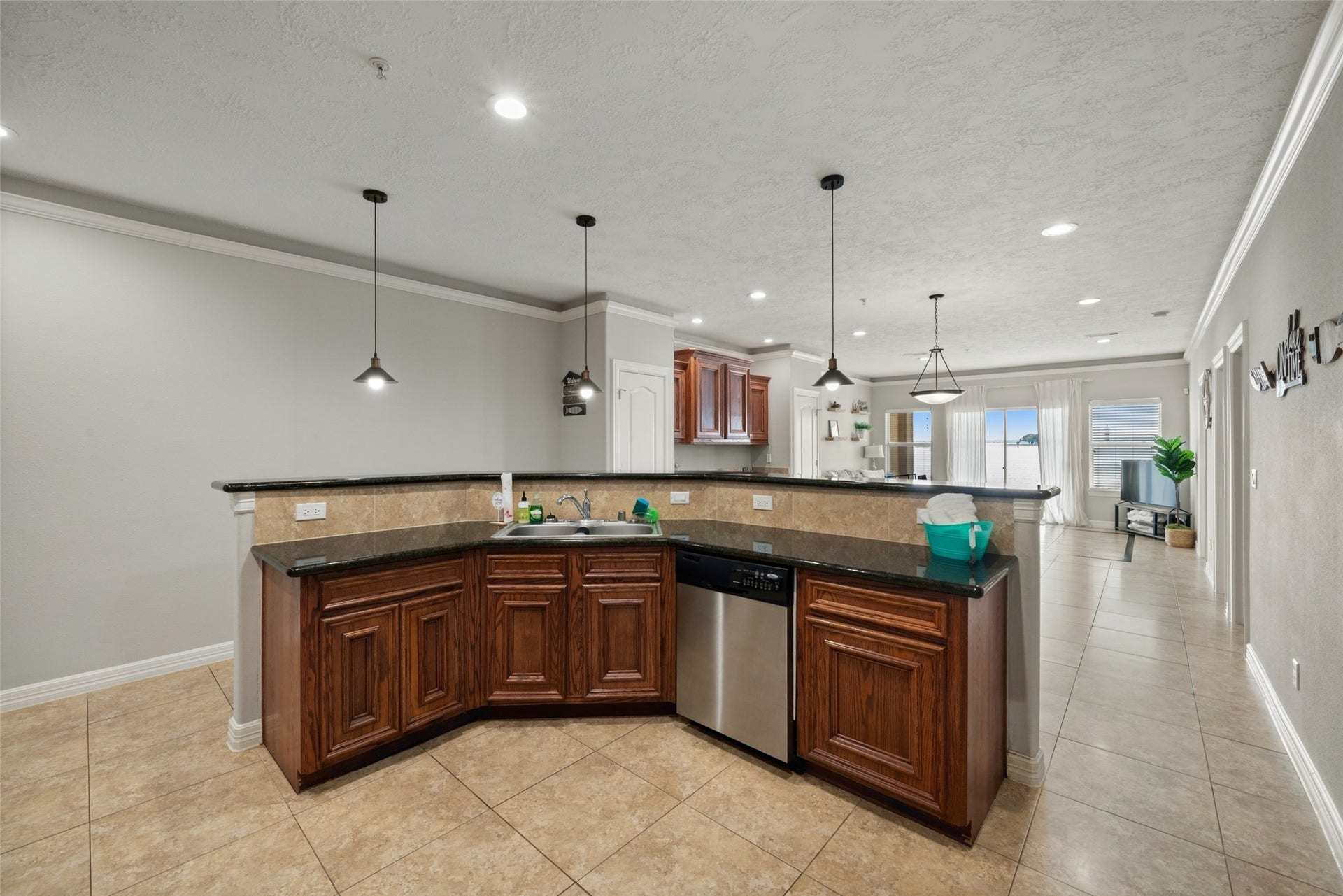 7037 Kingston Cove, #114, Willis, TX 77318 Wraparound kitchen features warm wood cabinetry, dark countertops, a dishwasher, and a raised breakfast bar accented by pendant lighting.