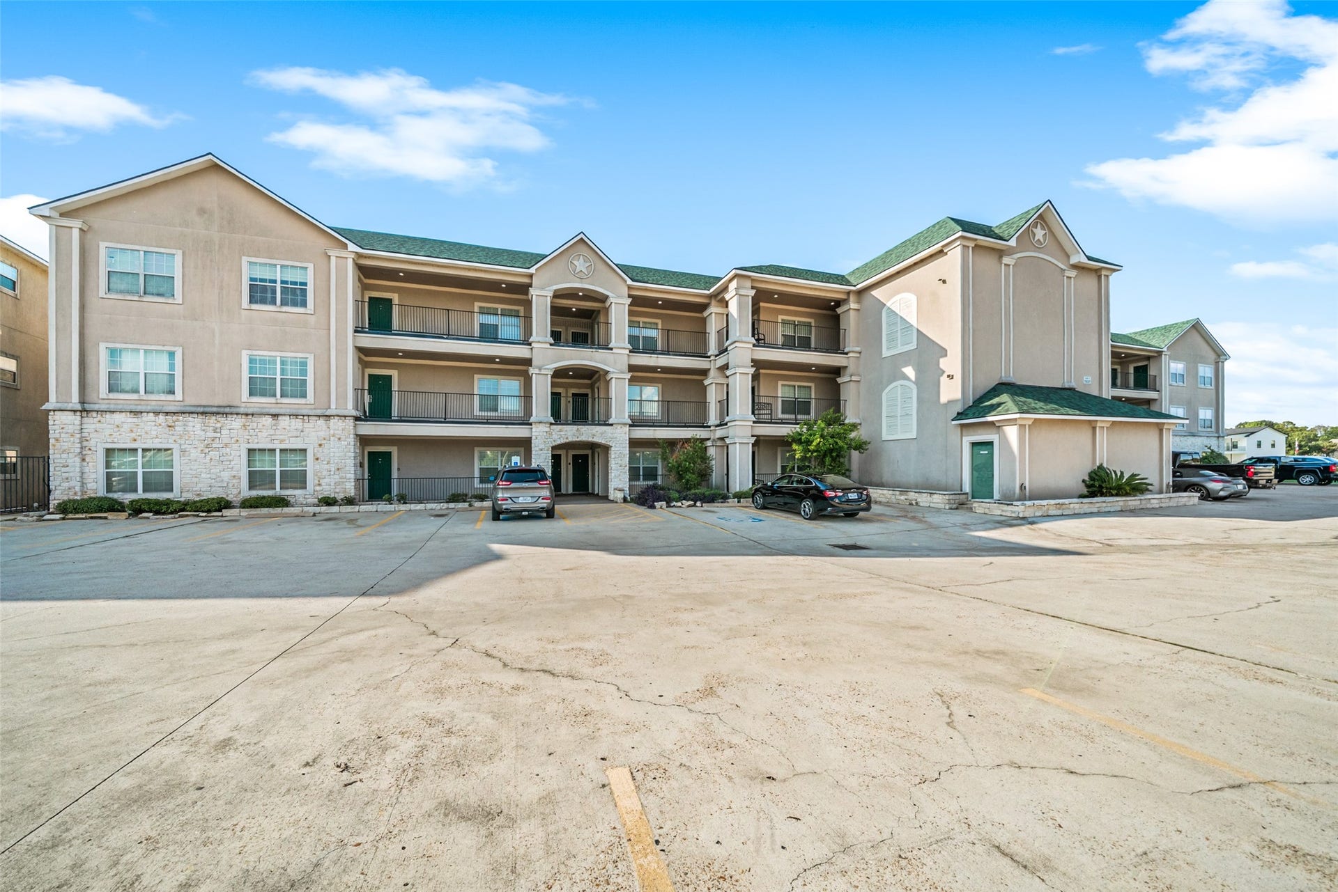 7037 Kingston Cove, #114, Willis, TX 77318 Exterior view of the condominium building featuring covered balconies, landscaped grounds, and a spacious paved parking area.