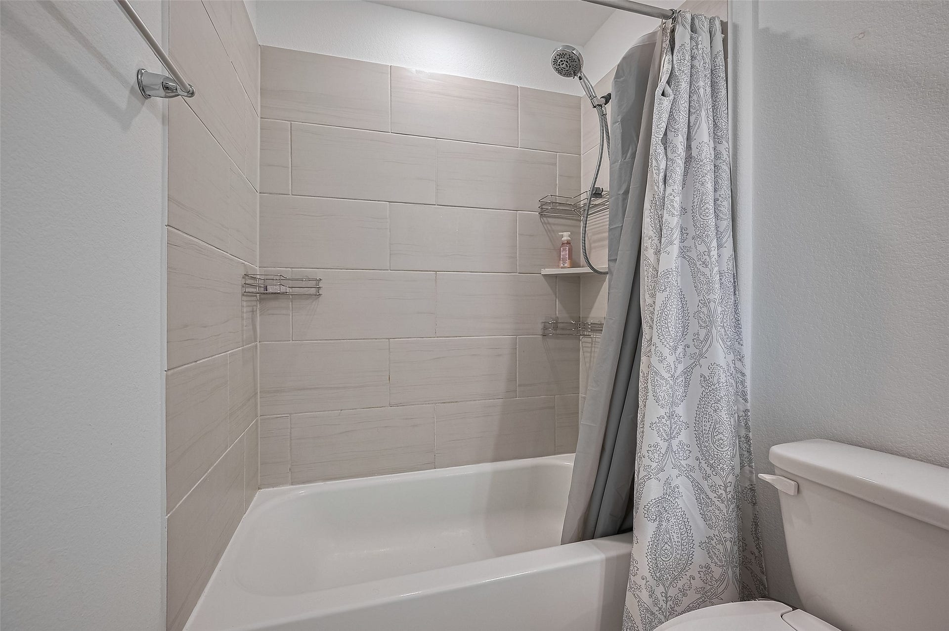 31326 Whitfield Court, Fulshear, TX 77441 A tiled shower and bathtub, featuring a patterned curtain and built-in shelves.