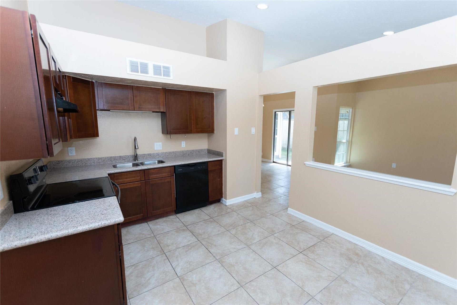 5610 Wallis Trail Court, Houston, TX 77049 Bright kitchen with dark wood cabinetry, sleek granite countertops, and modern appliances, opening to a spacious living area through a convenient pass-through window.
