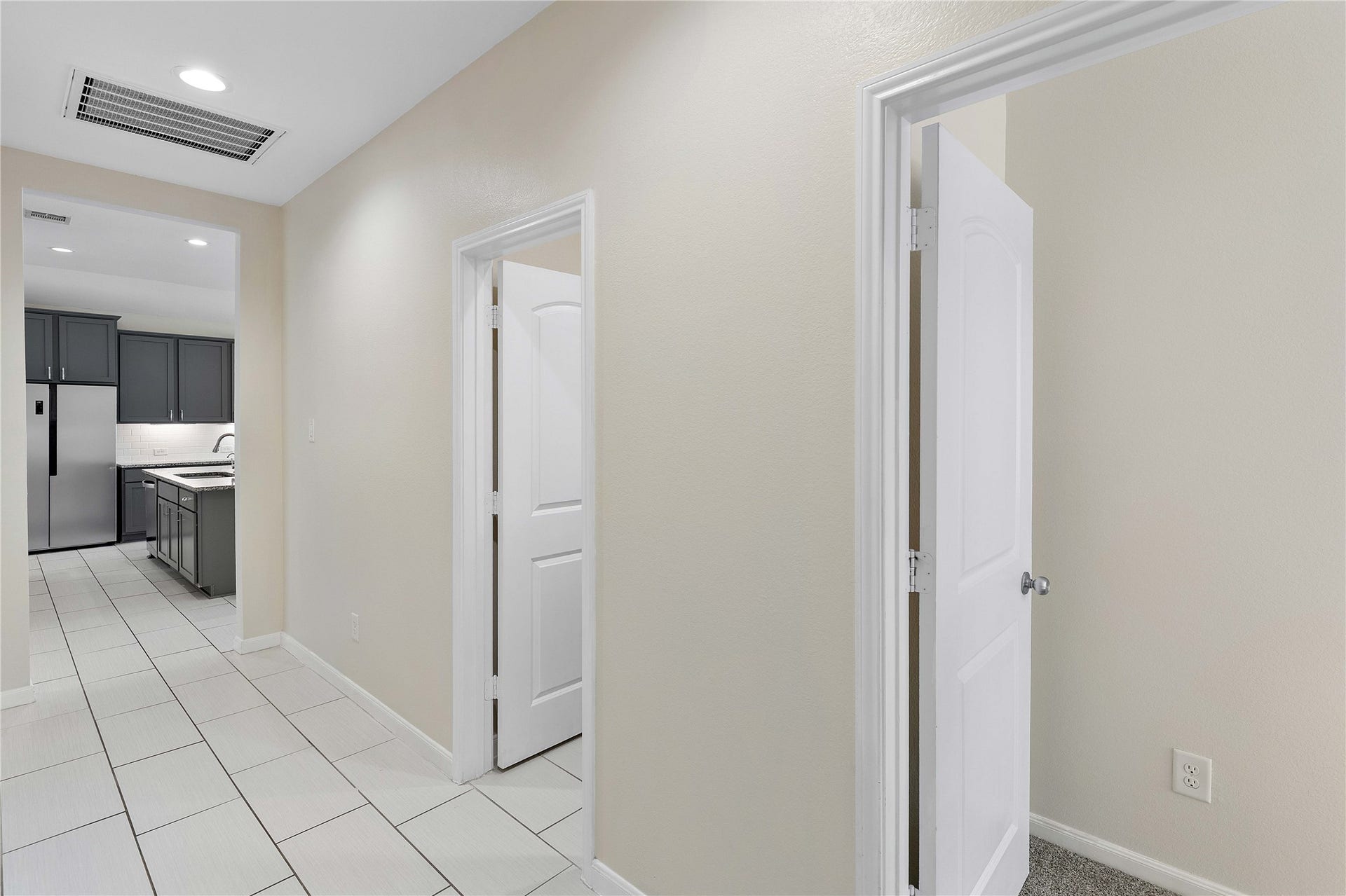 Bright hallway leads to a modern kitchen featuring sleek gray cabinetry and stainless steel appliances, offering a functional and stylish space.