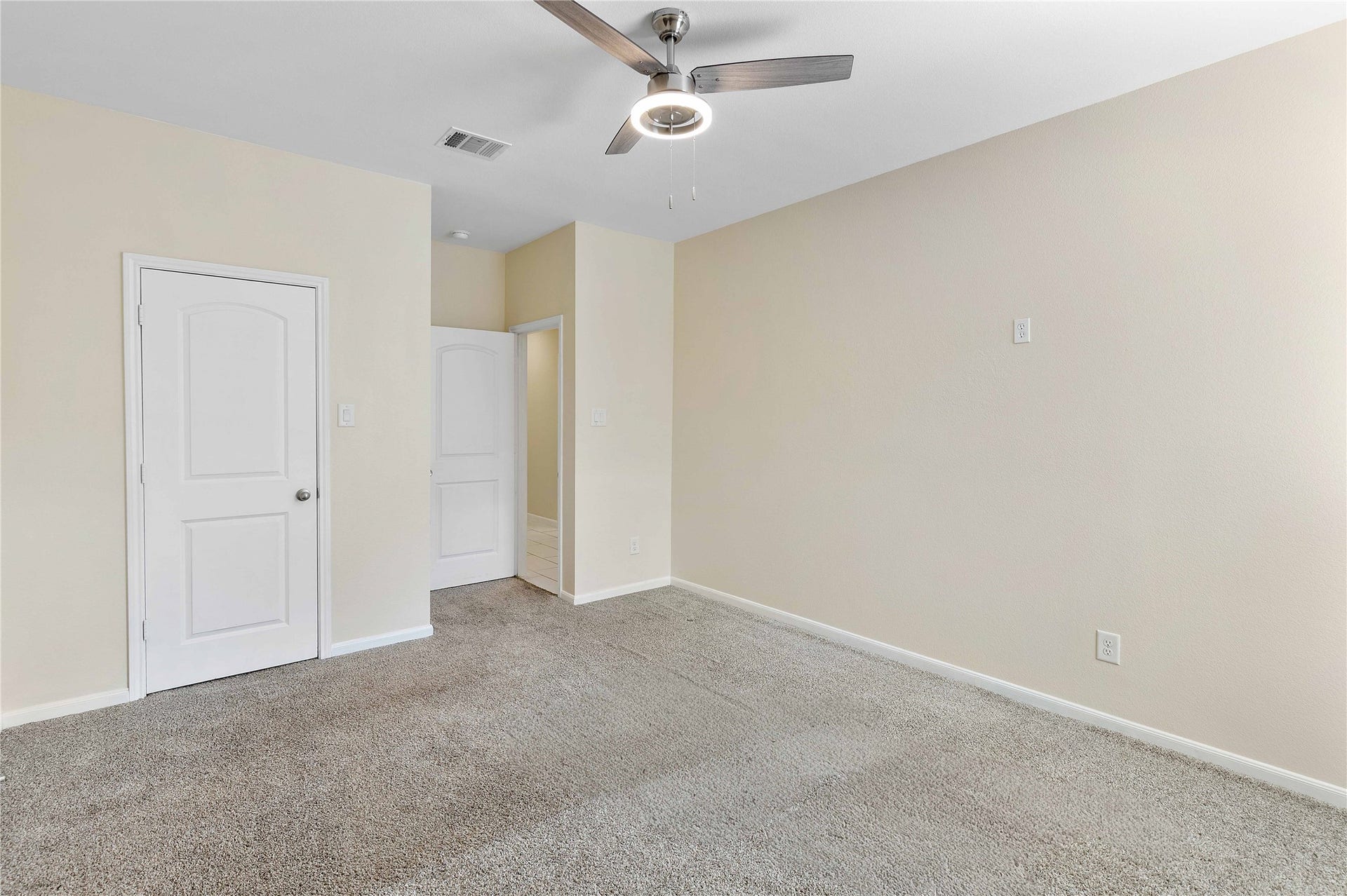 Spacious room with plush carpeting, neutral walls, and a modern ceiling fan, perfect for personalization and comfort.